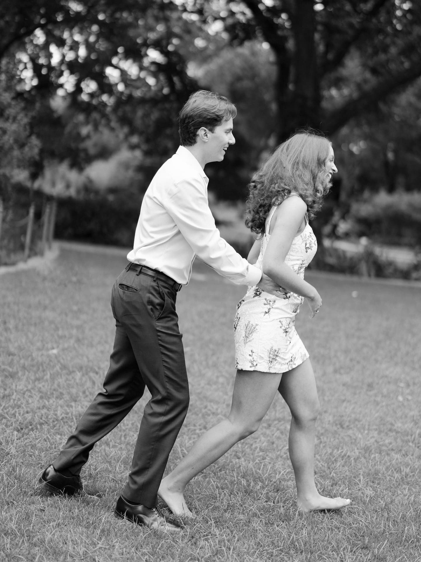 Fall engagement photos of a couple laughing mid-stride as he playfully pulls her close across a grassy lawn.