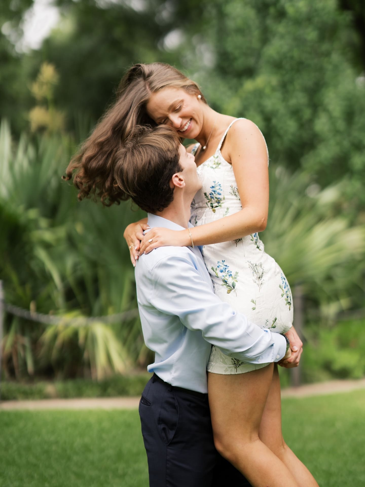 Fall engagement photos of a groom lifting his bride-to-be joyfully in a garden.