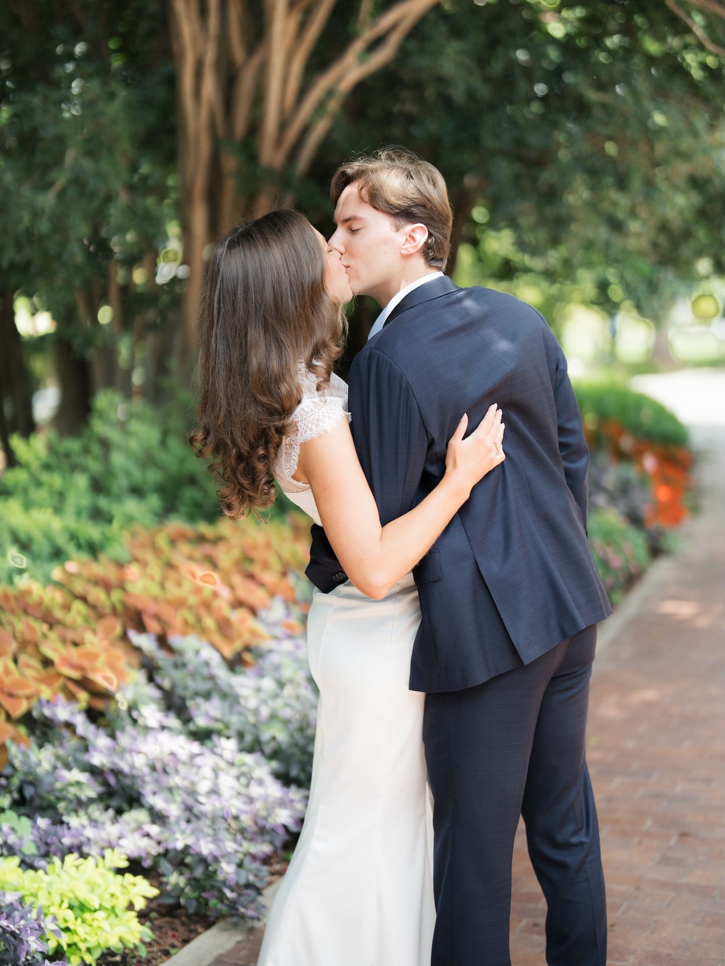 Fall engagement photos of a couple kissing beside vivid red and purple flower beds.