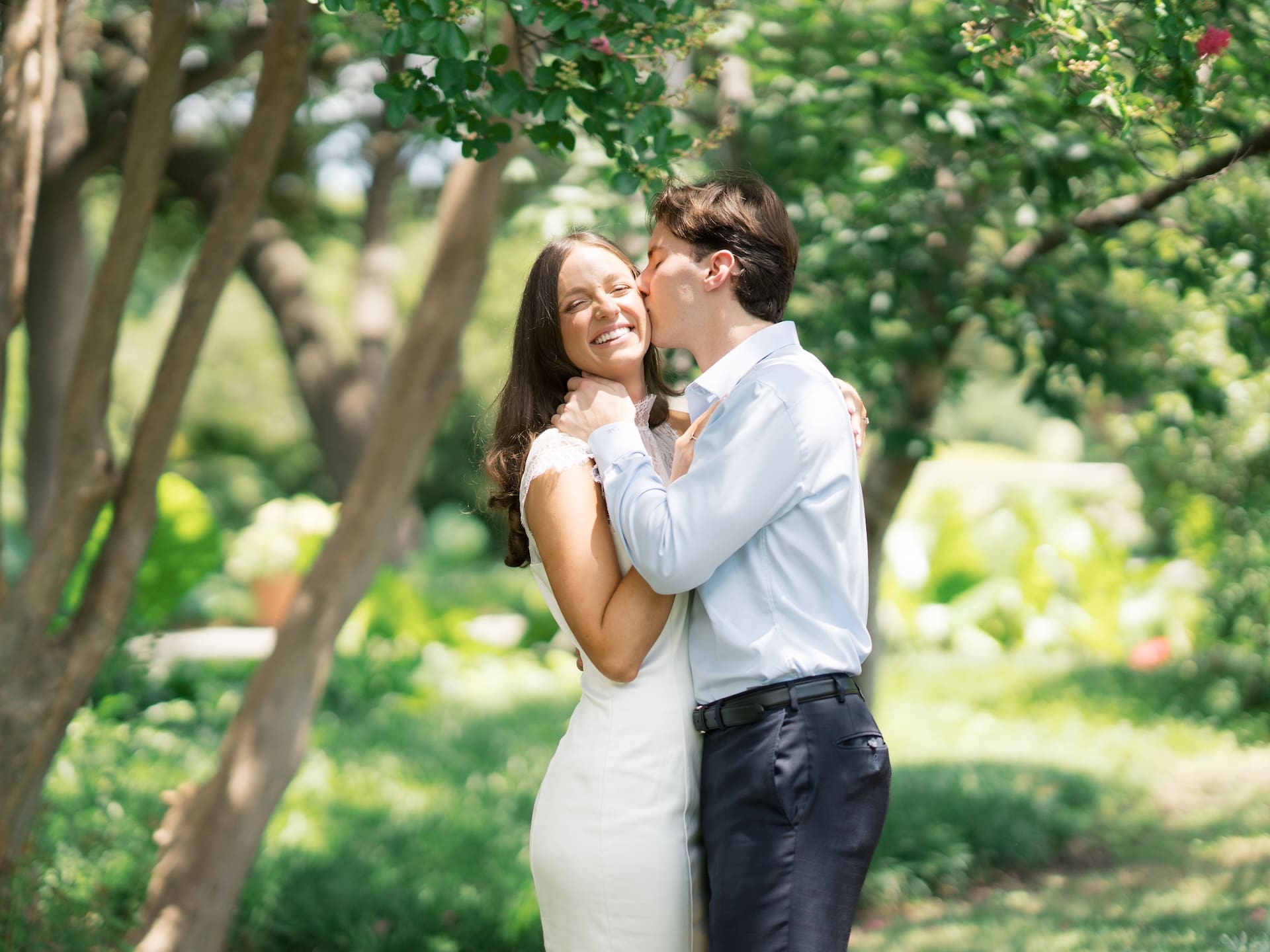 Fall engagement photos of a groom kissing his bride-to-be's cheek beneath flowering trees.
