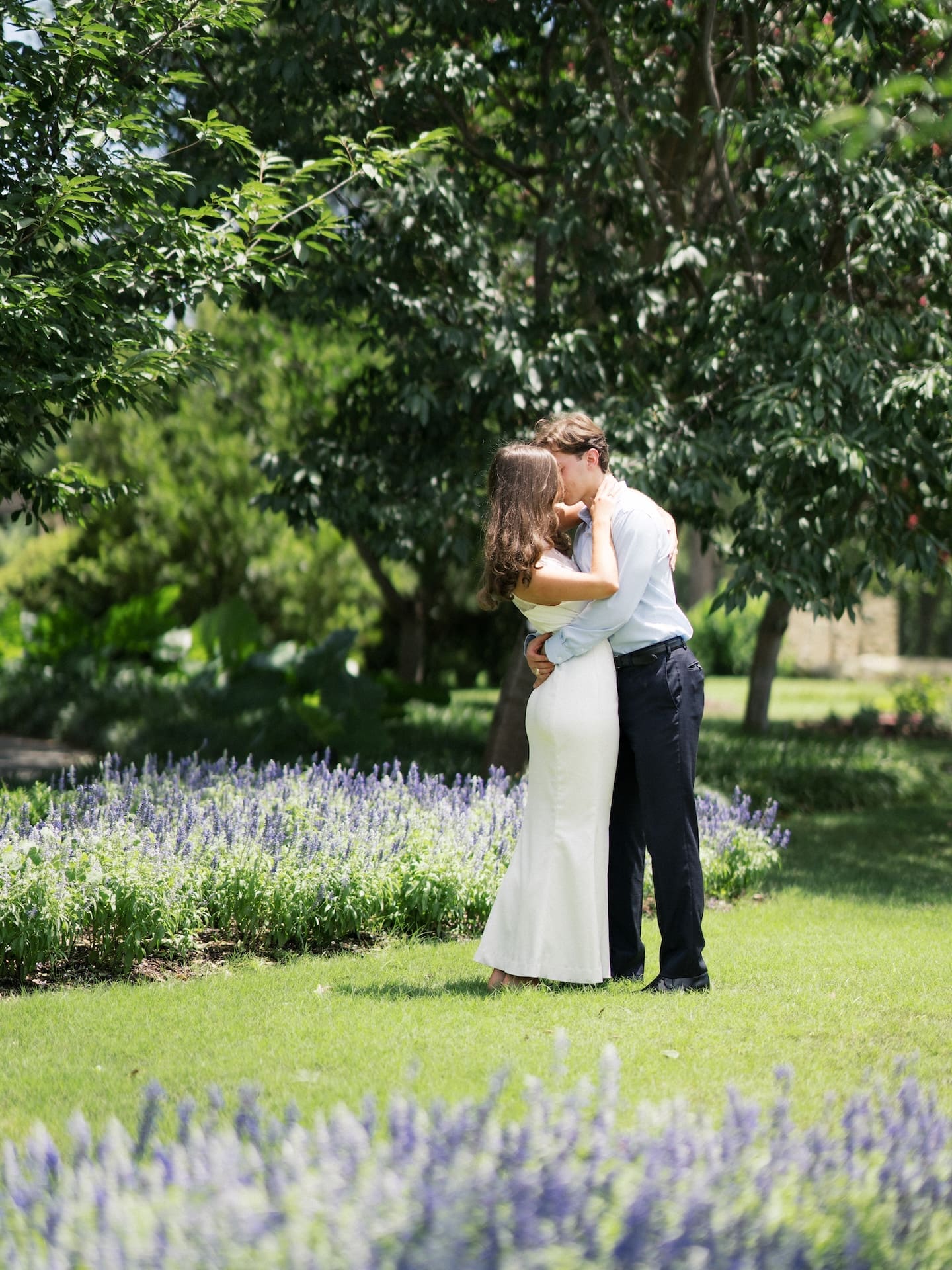Couple kissing while standing among blooming lavender in a garden.