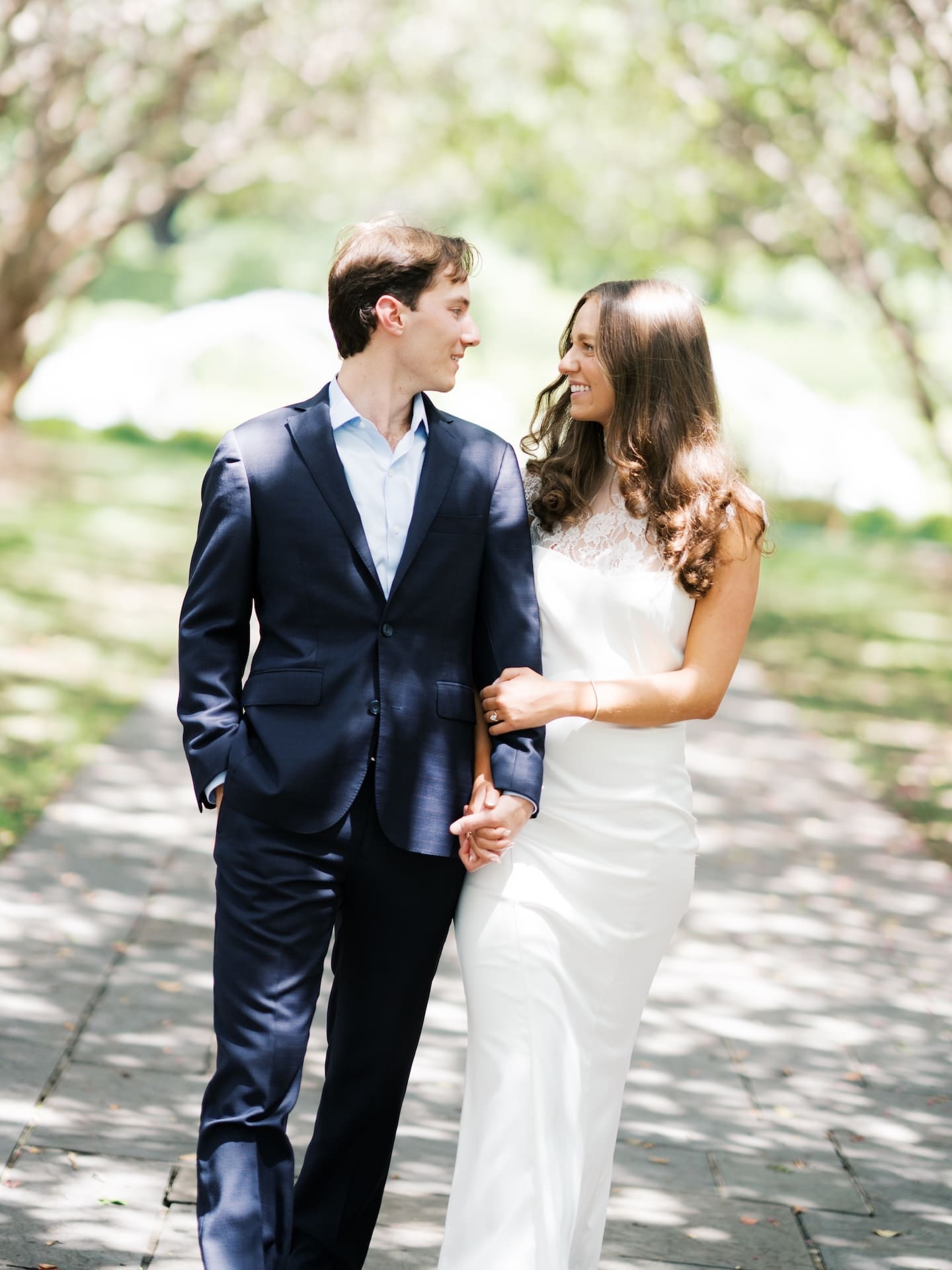 Fall engagement photos of a couple smiling and holding hands on a sunlit path.