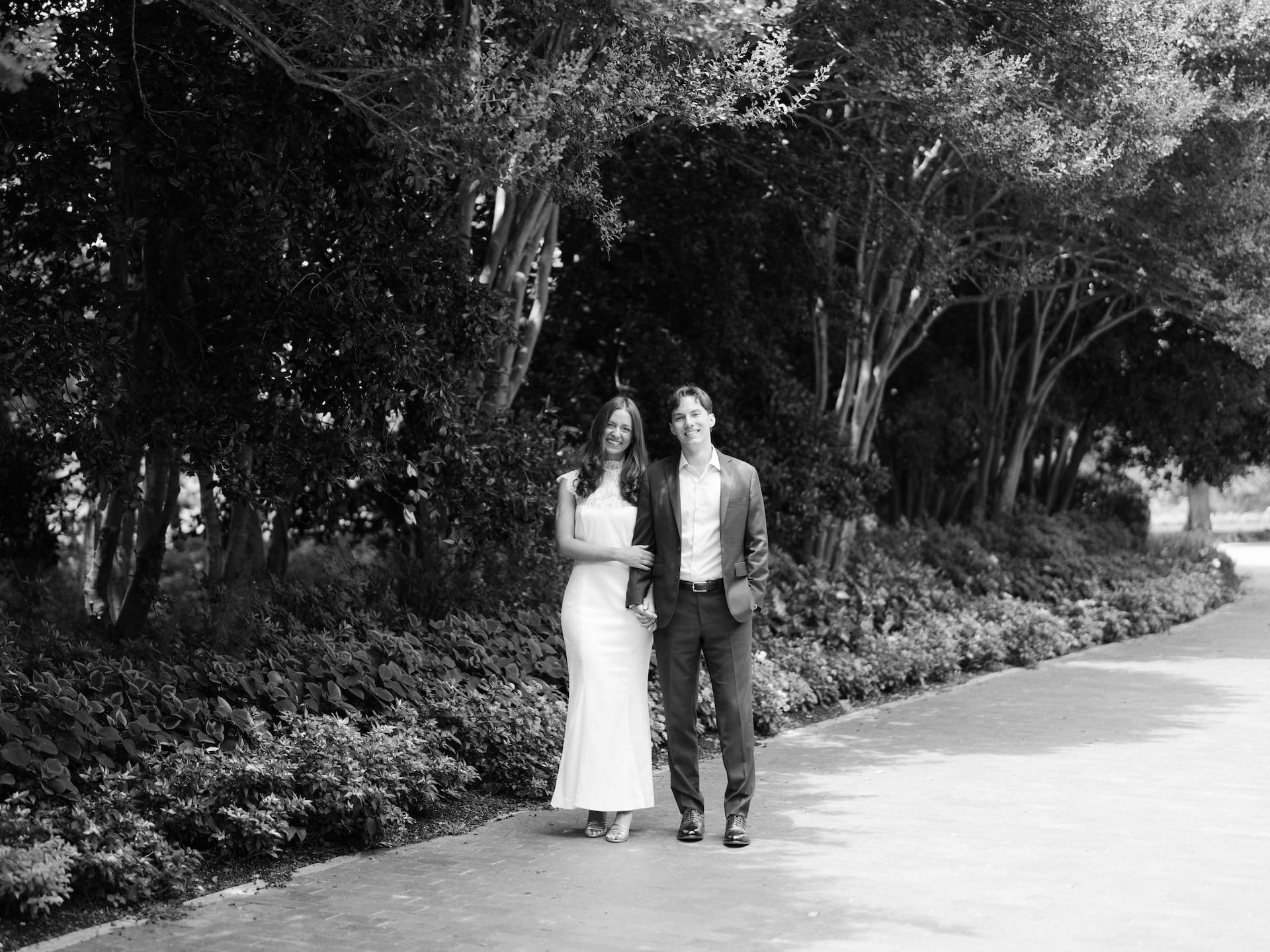 Couple smiling warmly together while standing on a shaded garden walkway.