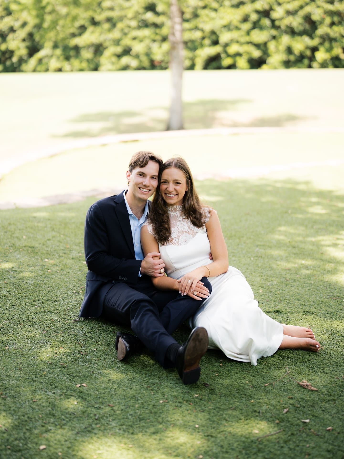 Couple sitting on the grass together, smiling with bare feet stretched out.