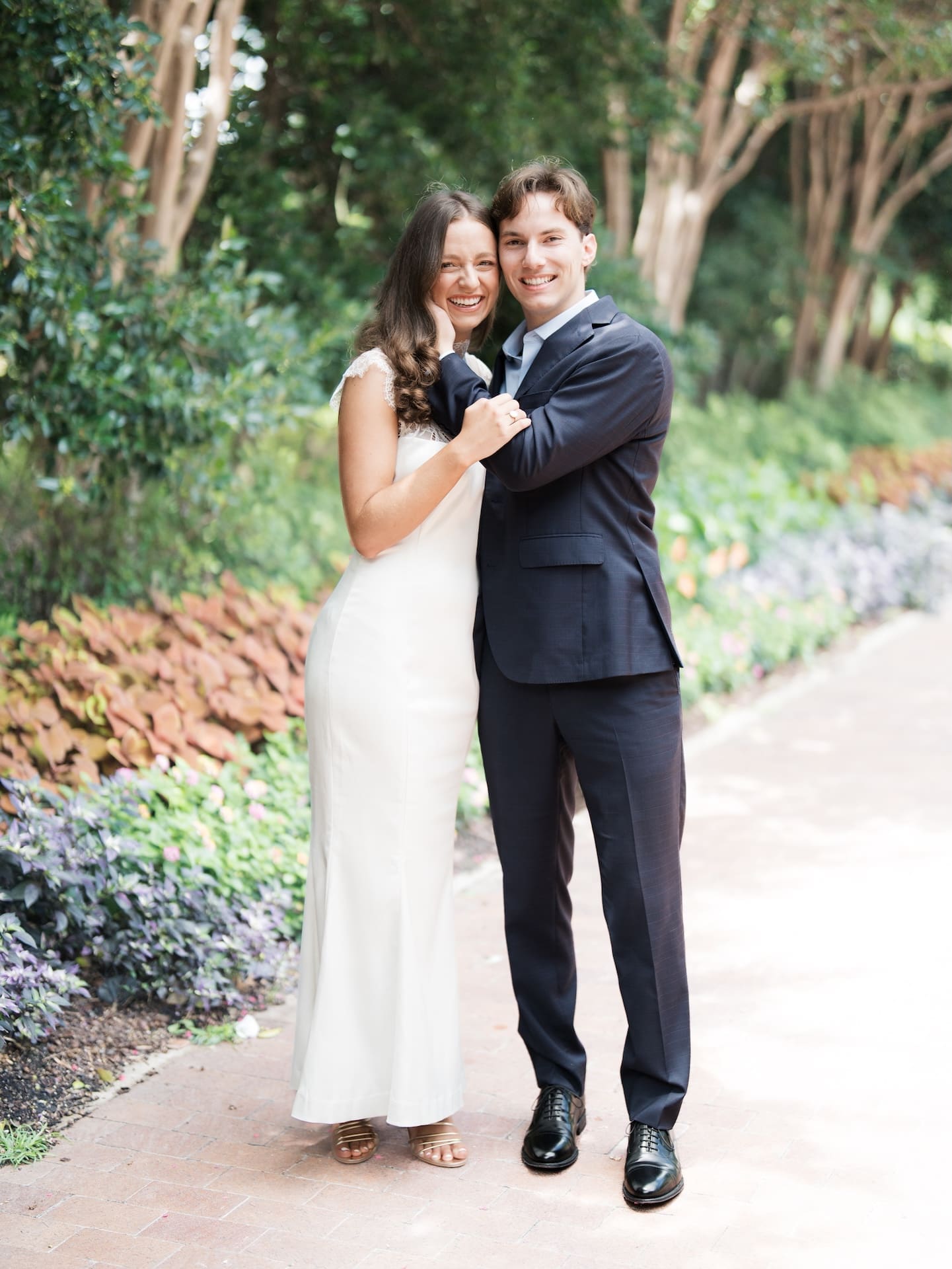 Fall engagement photos of a couple smiling cheek-to-cheek along a flower-lined garden path.