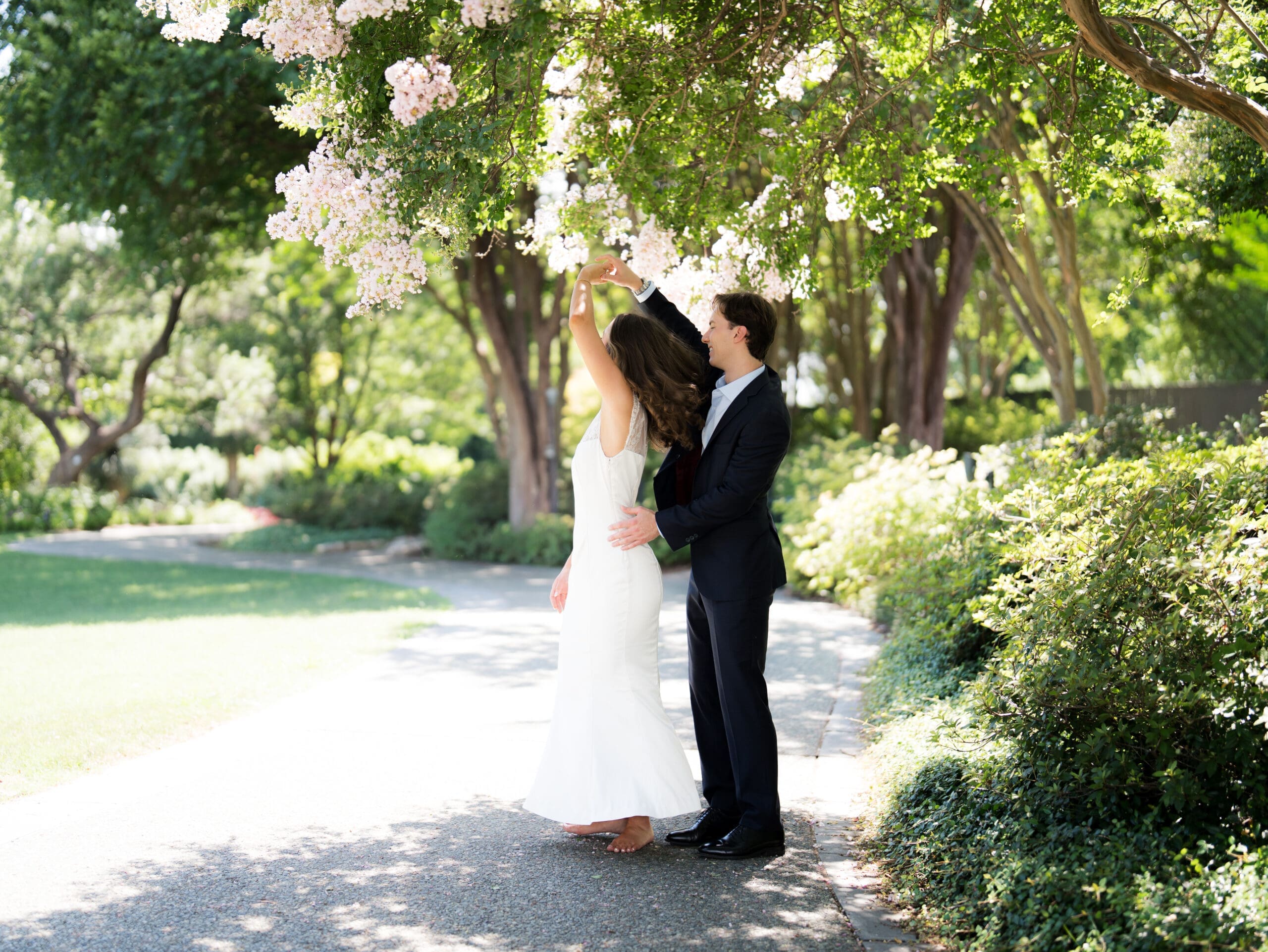 Groom twirling his bride-to-be beneath a canopy of pink blossoms.