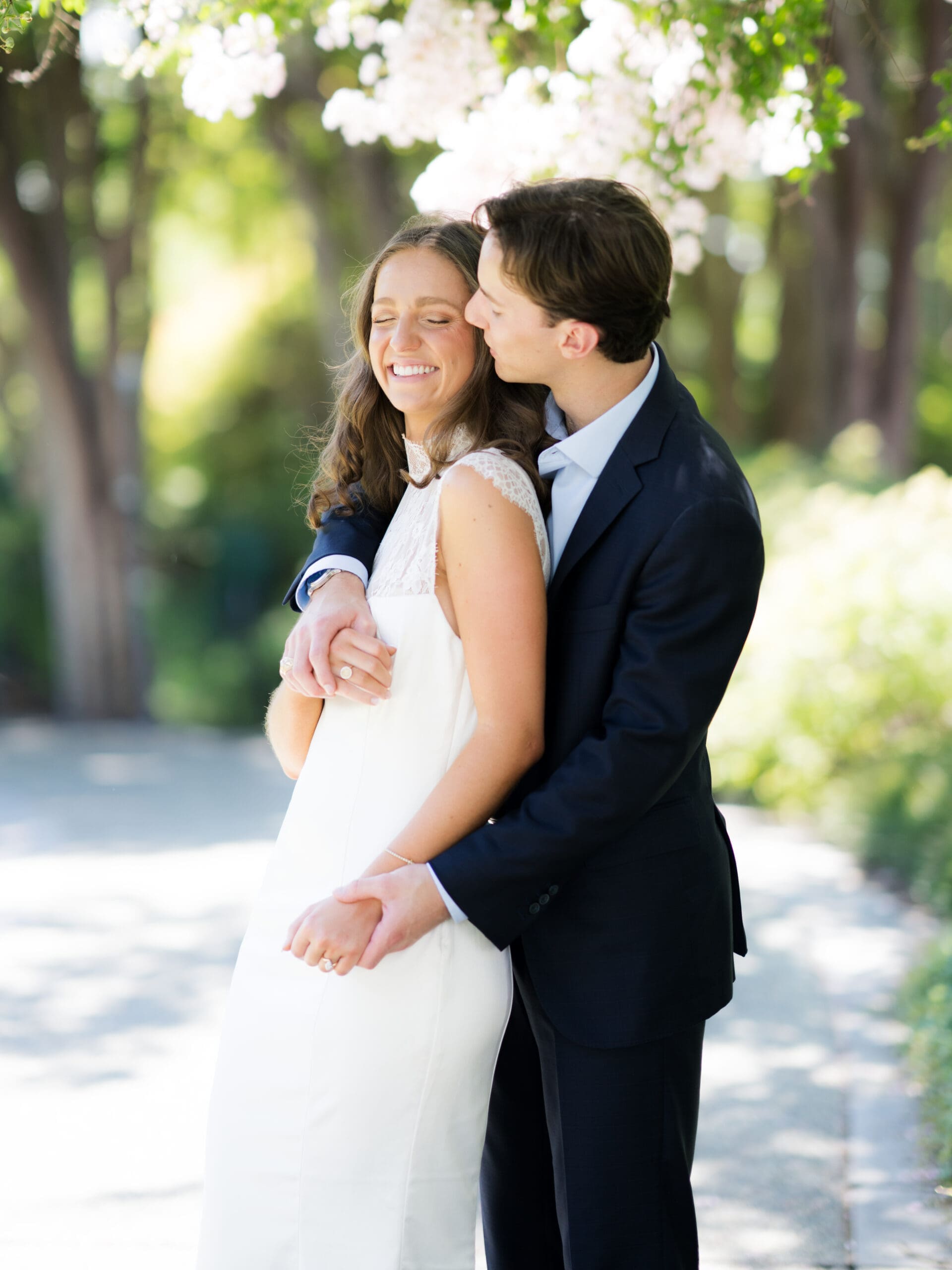 Fall engagement photos of a groom kissing his bride-to-be's cheek under blossoming trees.
