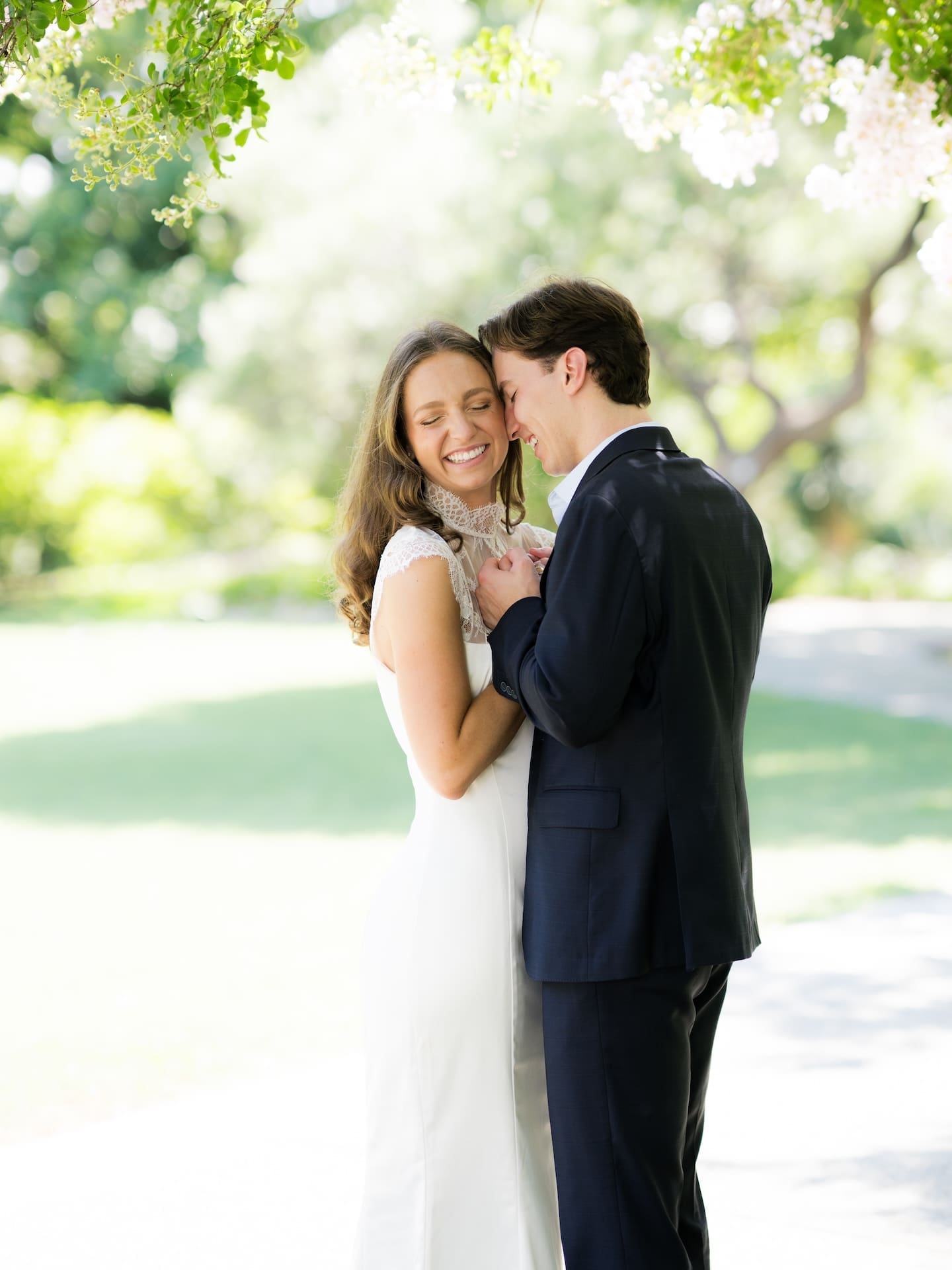 Couple nuzzling close together, laughing softly under dappled sunlight.