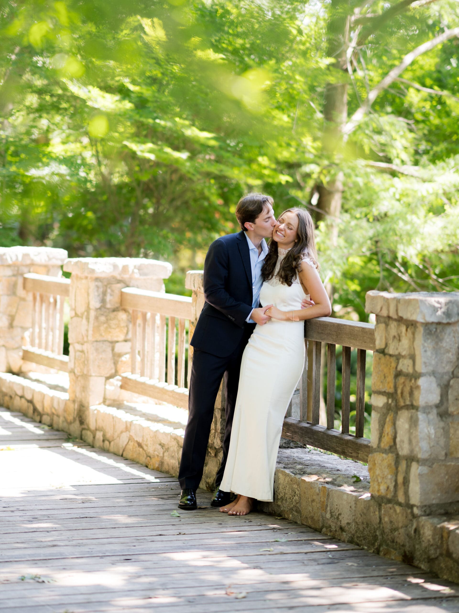 Fall engagement photos of a couple kissing on a stone bridge in a shaded garden.