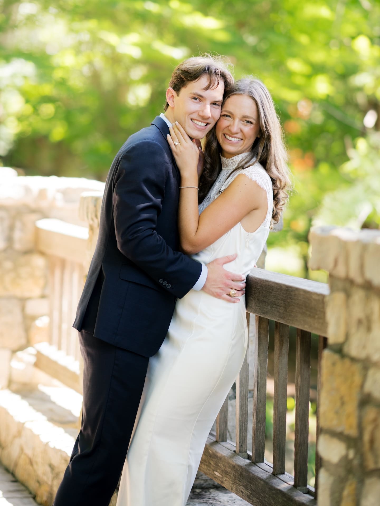 Fall engagement photos of a couple smiling together while leaning against a rustic stone bridge railing.