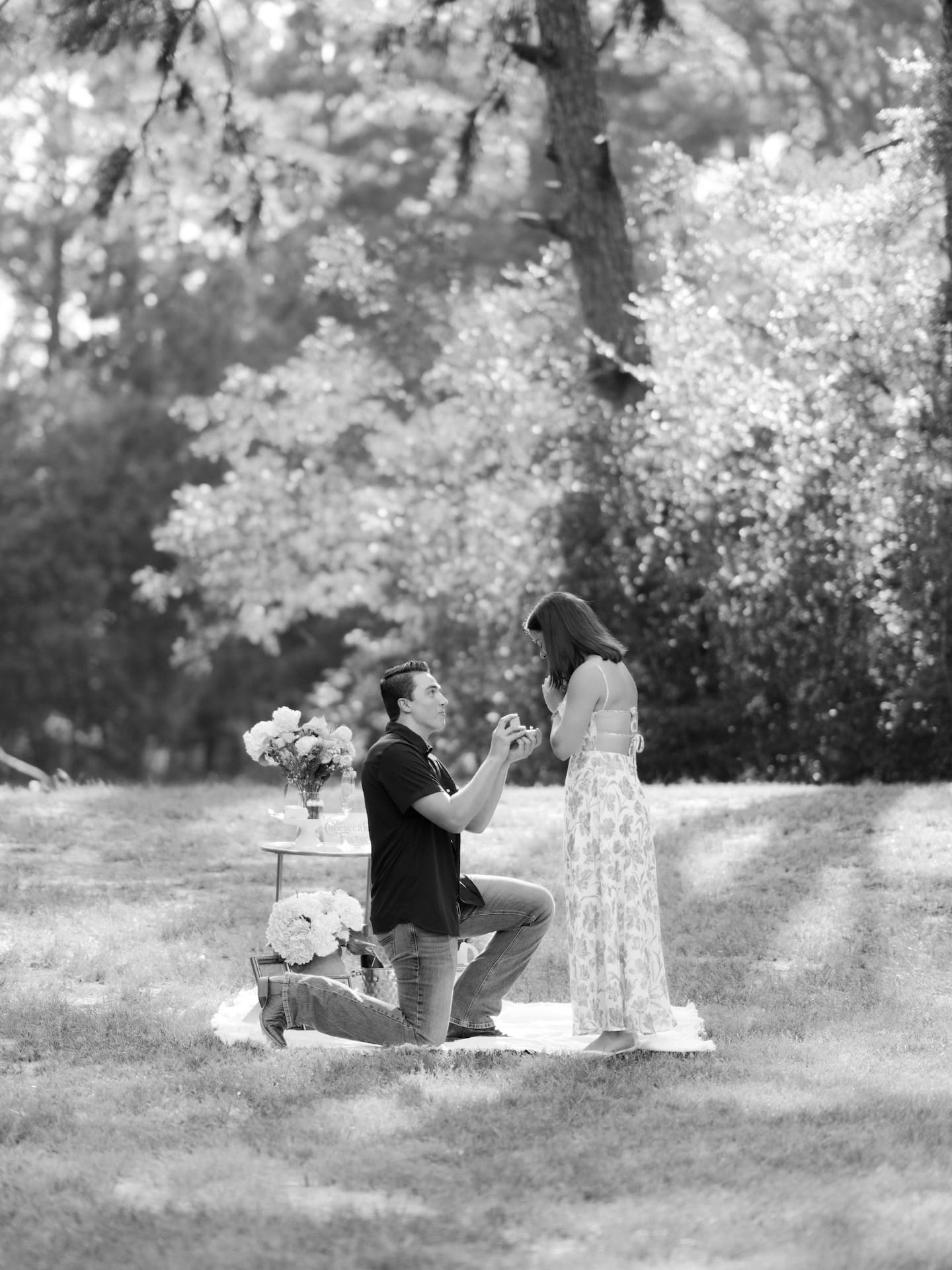 Surprise Engagement Proposal Ideas showing a man on one knee proposing in a wooded field, captured in black and white.