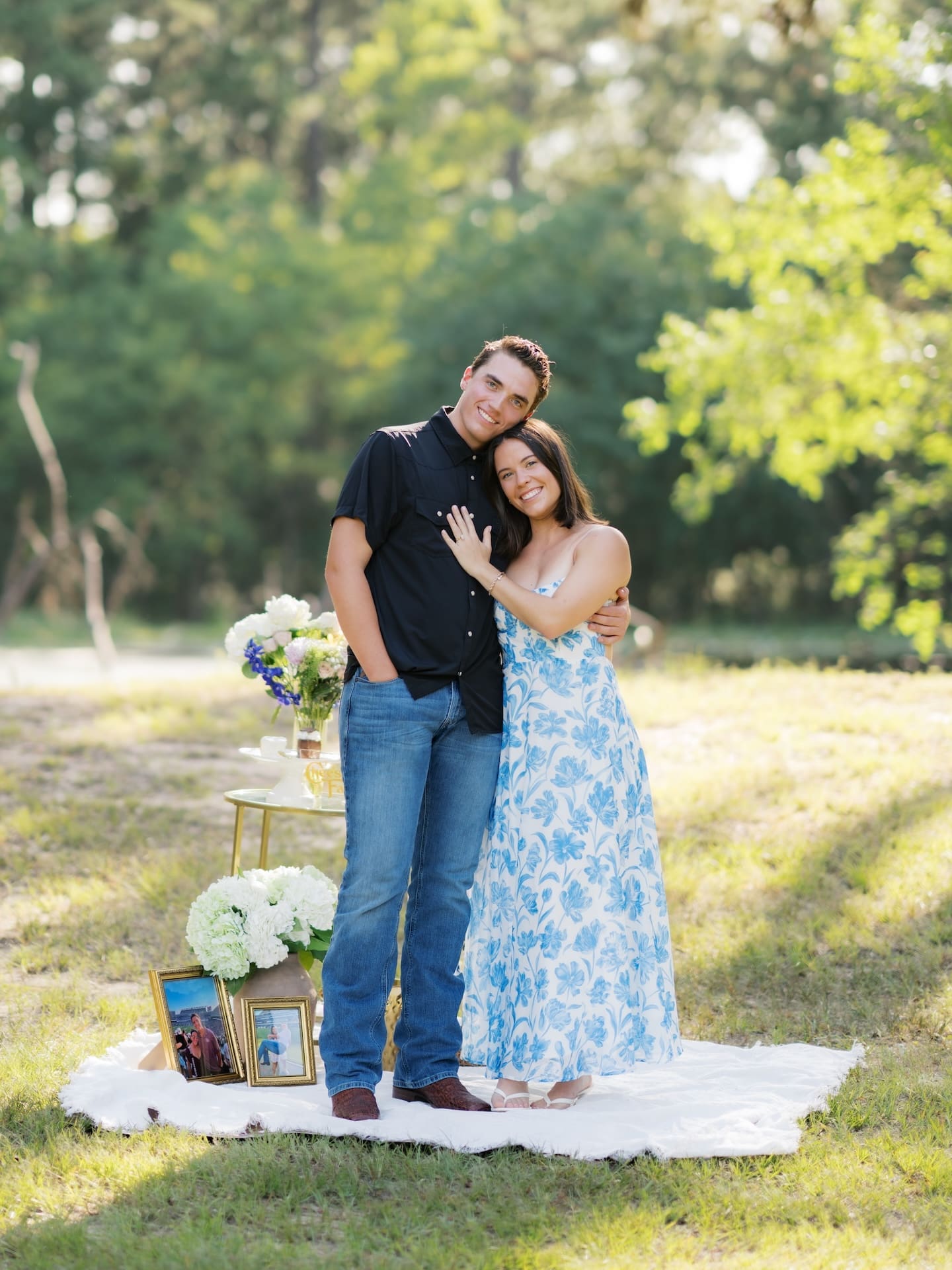 Newly engaged couple embracing warmly beside their decorated picnic setup.