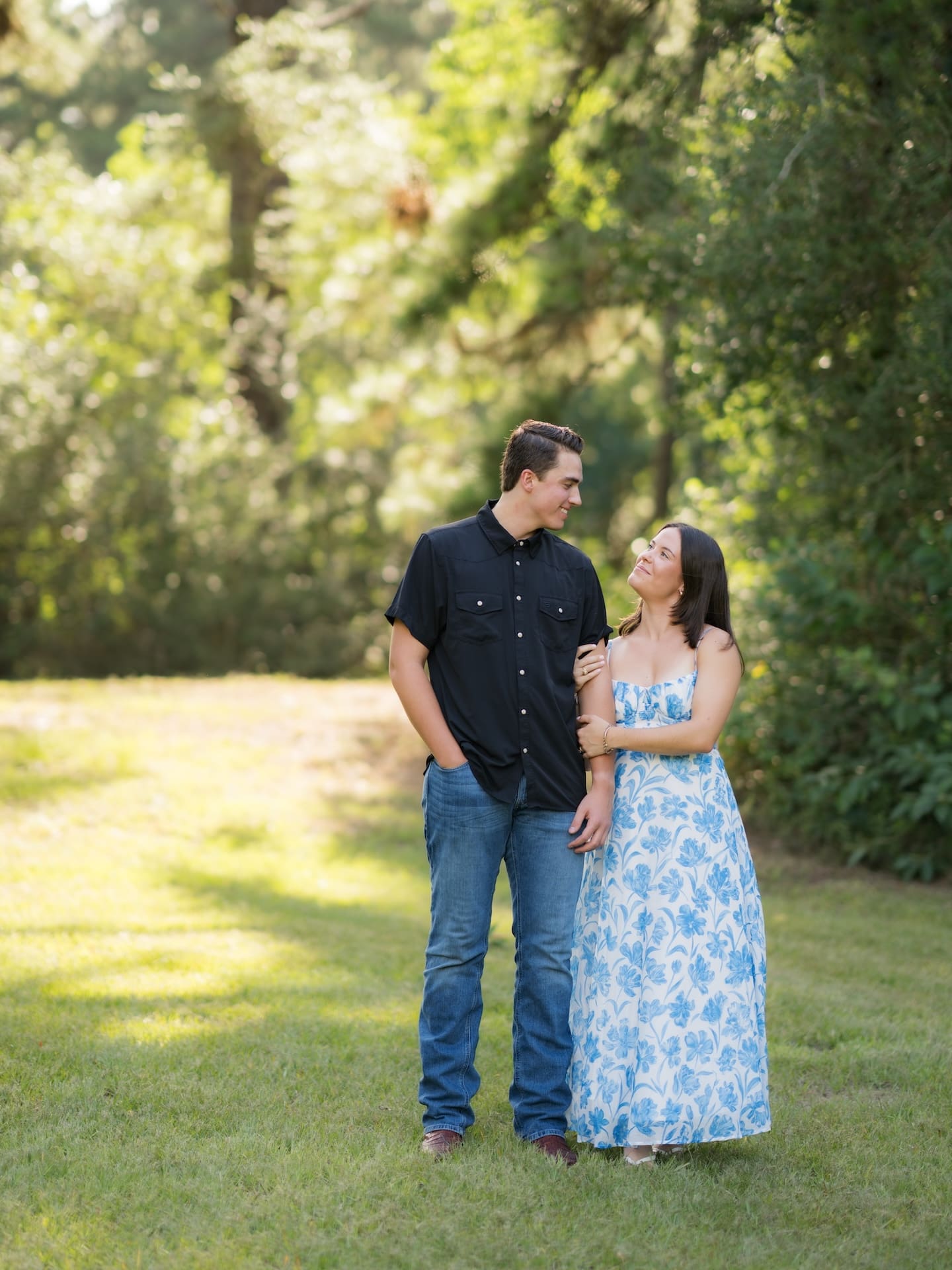 Surprise Engagement Proposal Ideas featuring a couple smiling at each other in a sunlit wooded area.