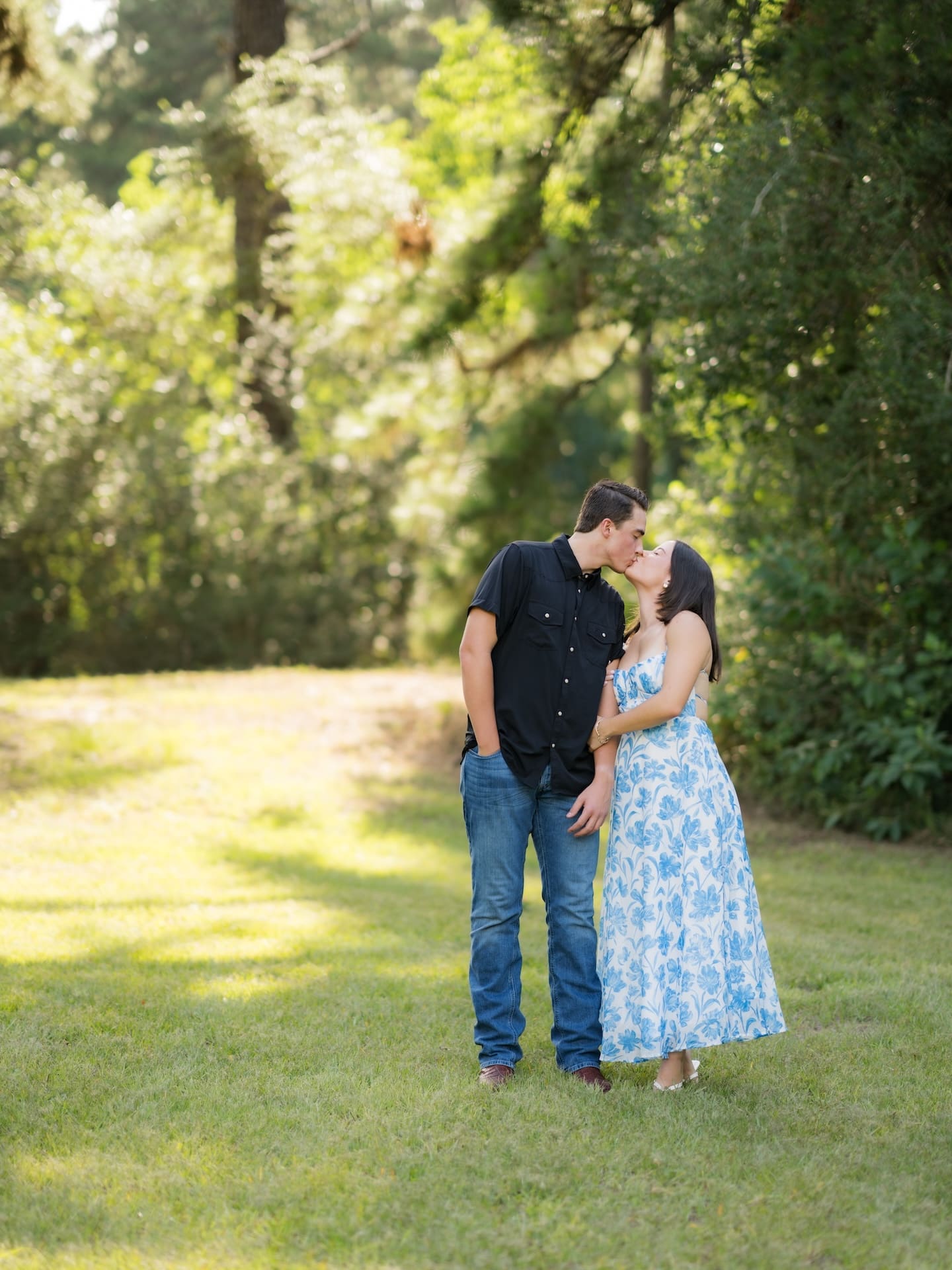 Couple sharing a kiss together in a sunlit wooded field.