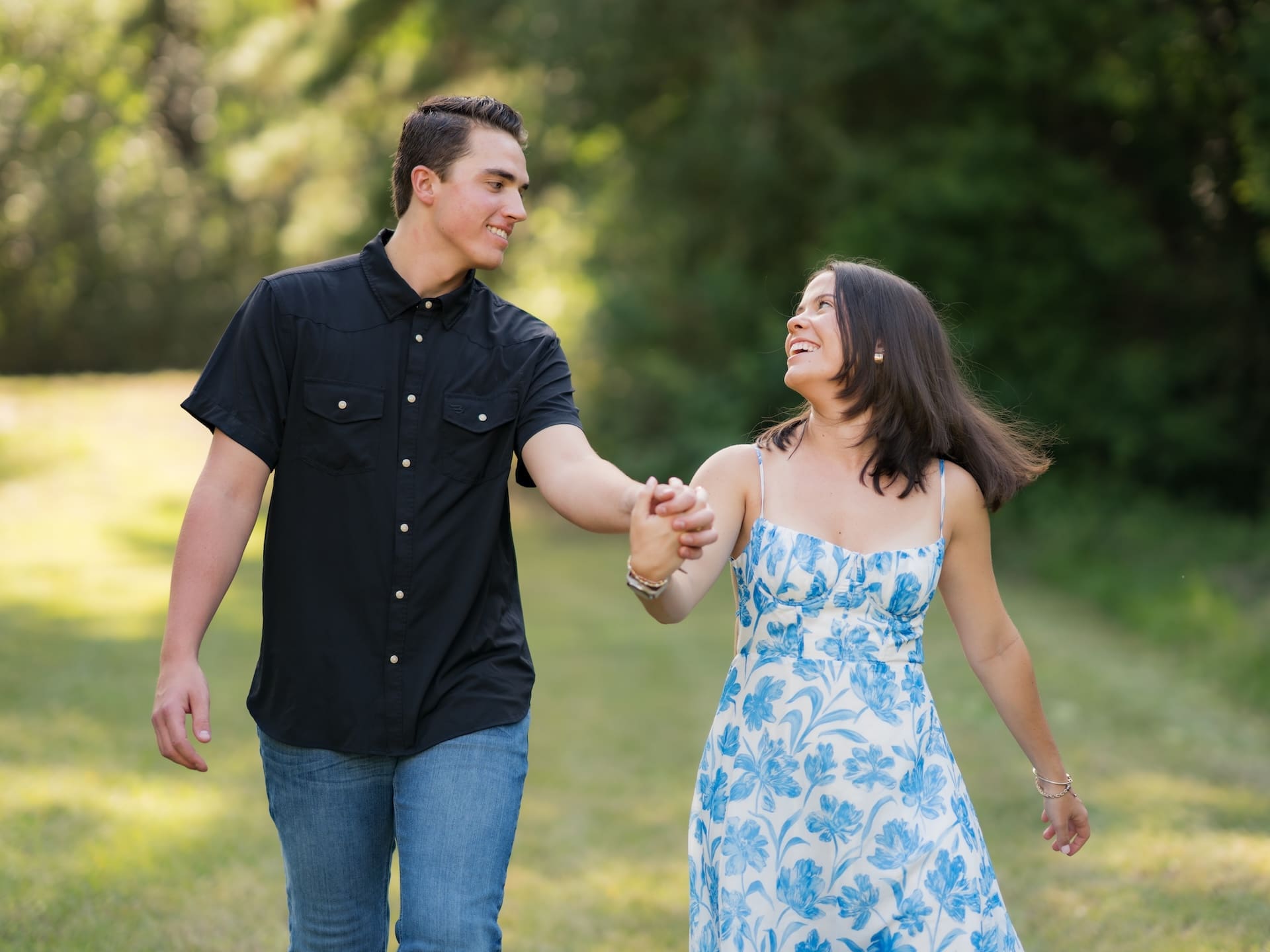 Newly engaged couple laughing and holding hands while walking together outdoors.