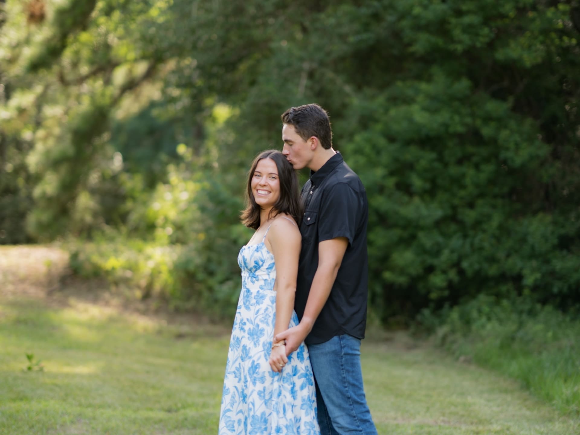 Surprise Engagement Proposal Ideas featuring a man kissing his fiancée's forehead in a sunlit field.