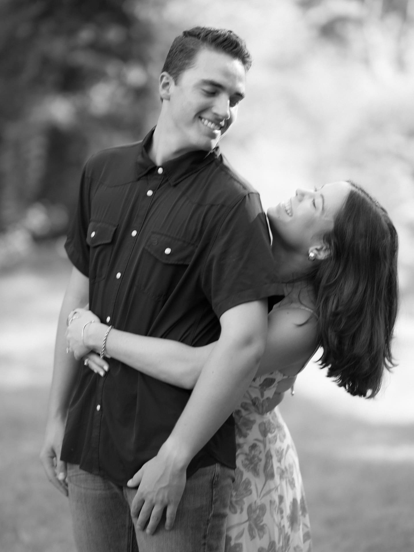 Newly engaged couple laughing together in black and white, her leaning back into his embrace.