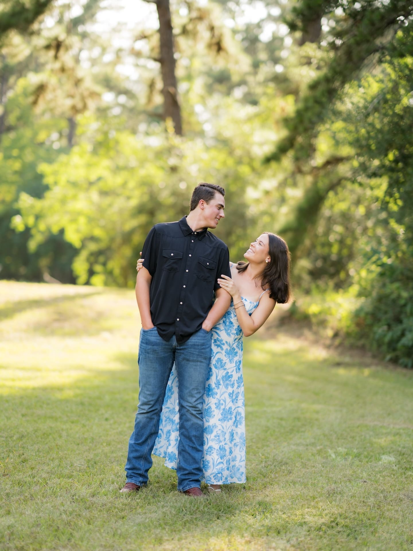 Couple smiling at each other while standing together in a sunlit field.