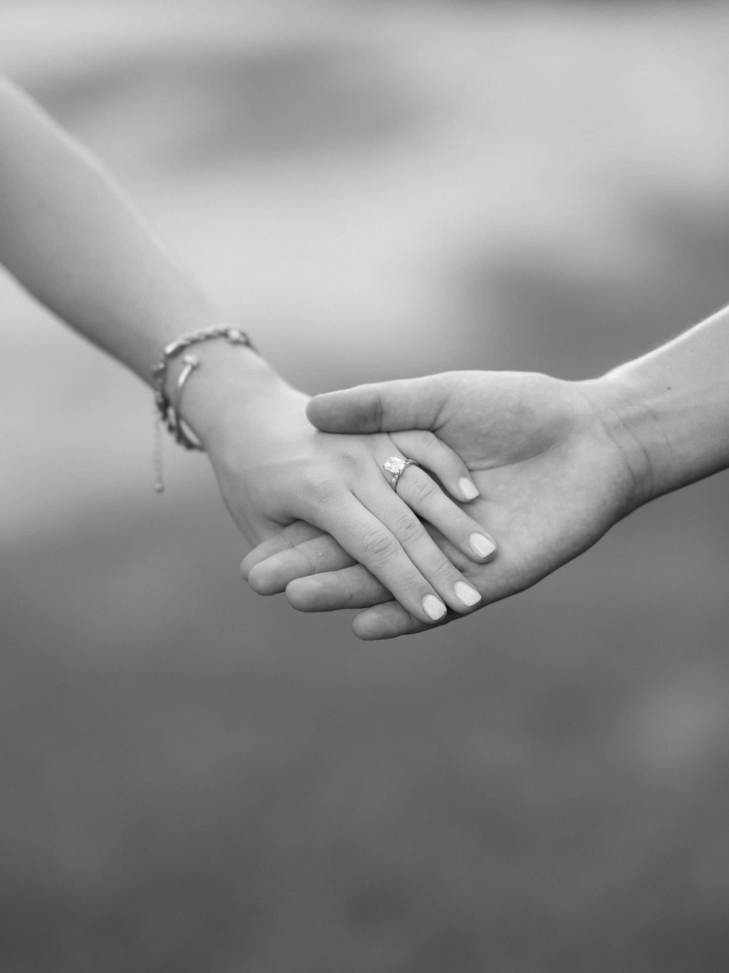 Black and white close-up of a couple holding hands, showing off a new engagement ring.