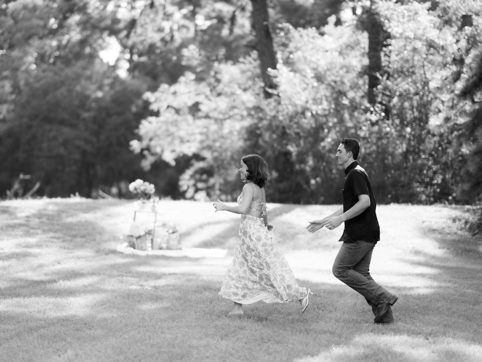 Newly engaged couple laughing as they run together across a grassy field in black and white.