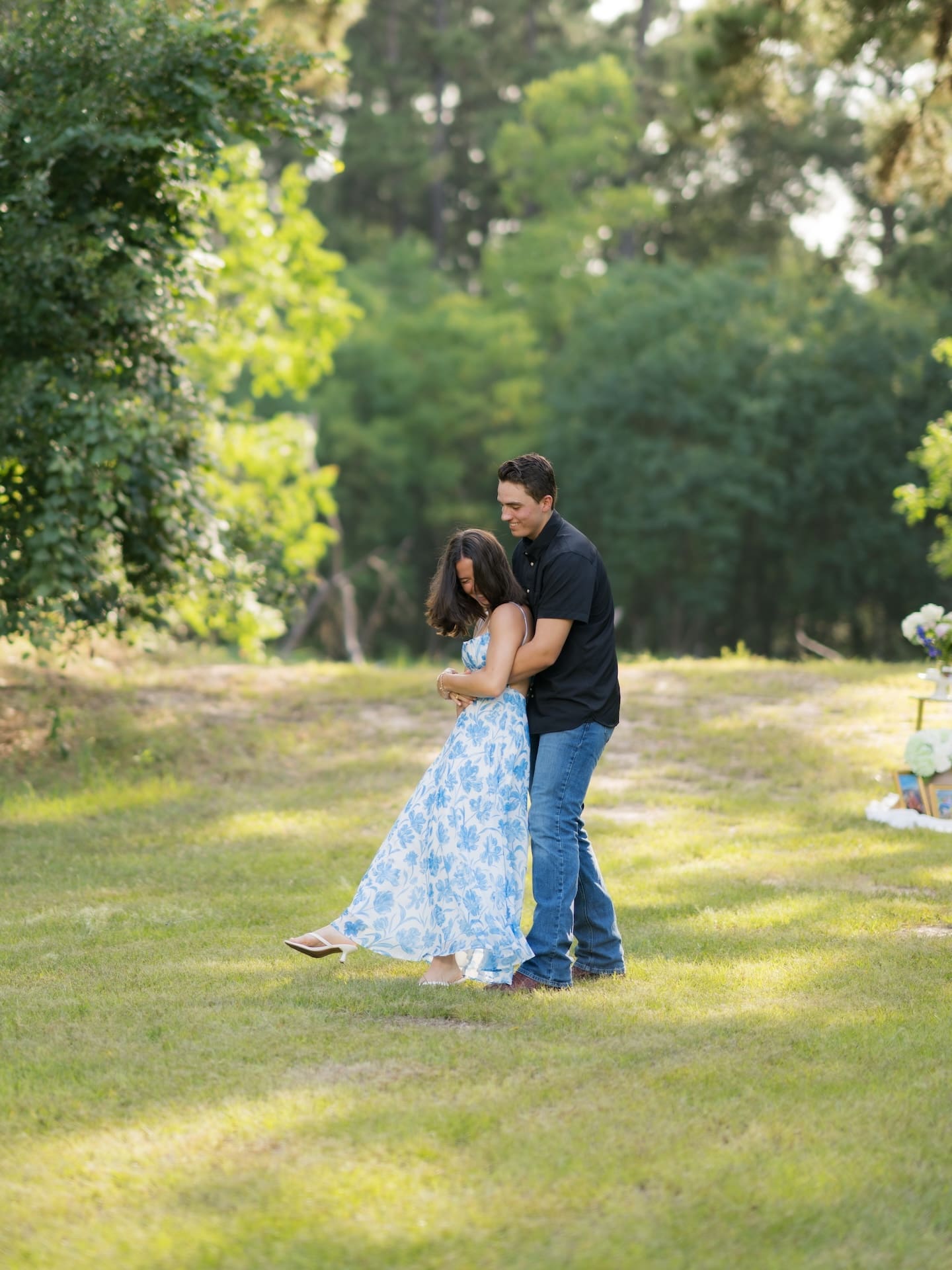 Newly engaged couple embracing and laughing together in a wooded field.
