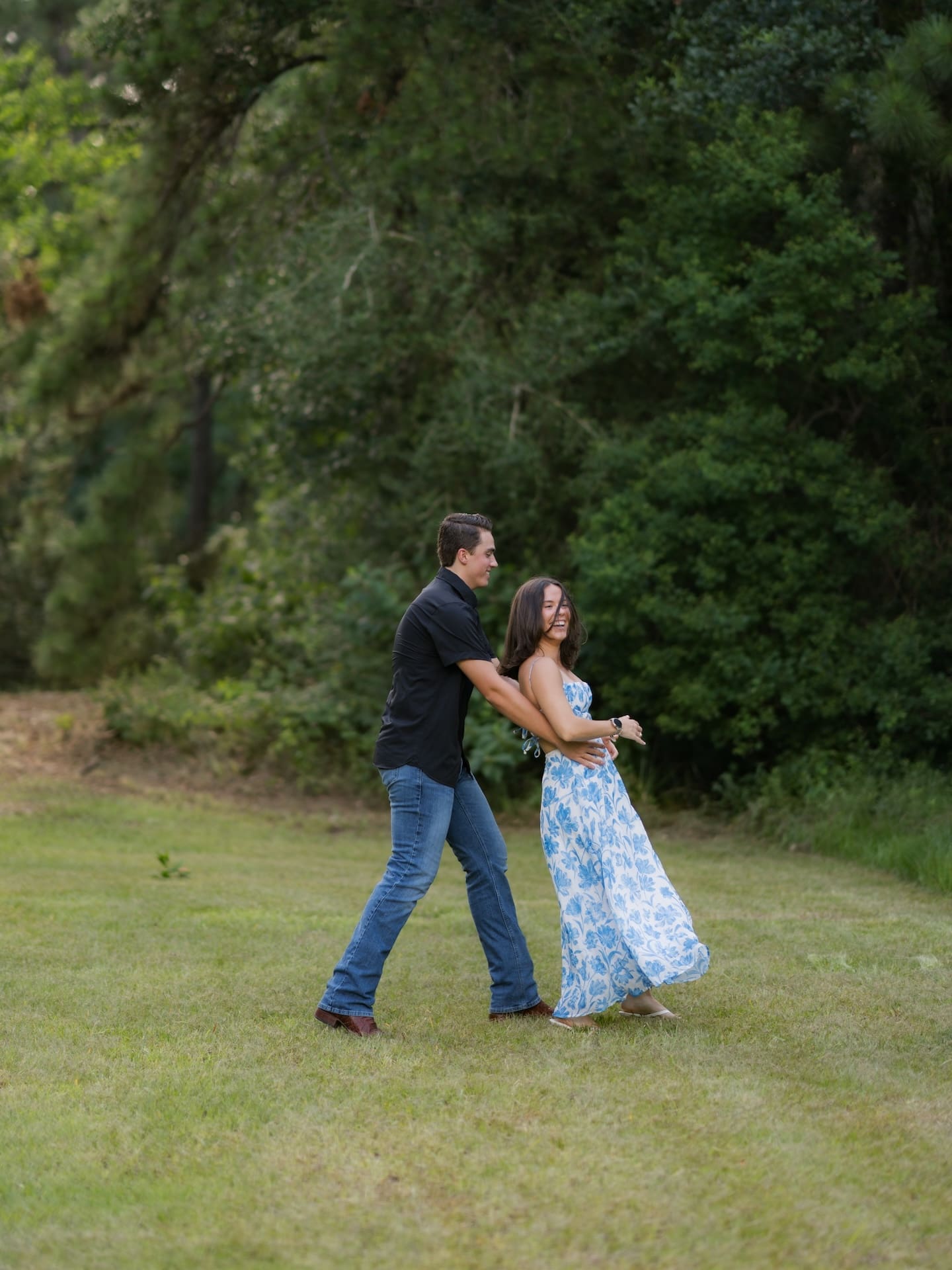 Surprise Engagement Proposal Ideas featuring a man playfully embracing his fiancée as they walk across a field.