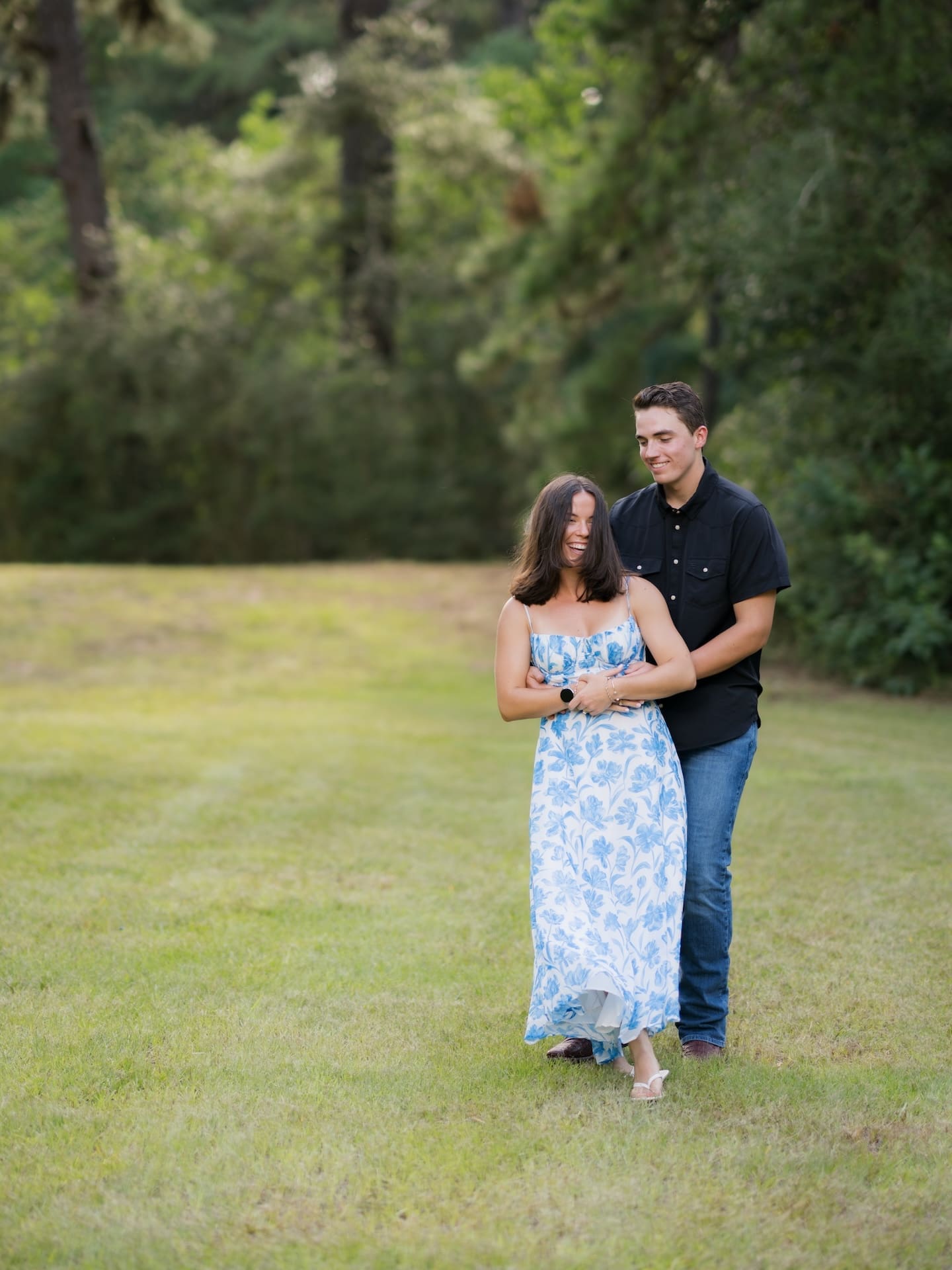 Couple walking together in a field, the man's arm wrapped around his fiancée.