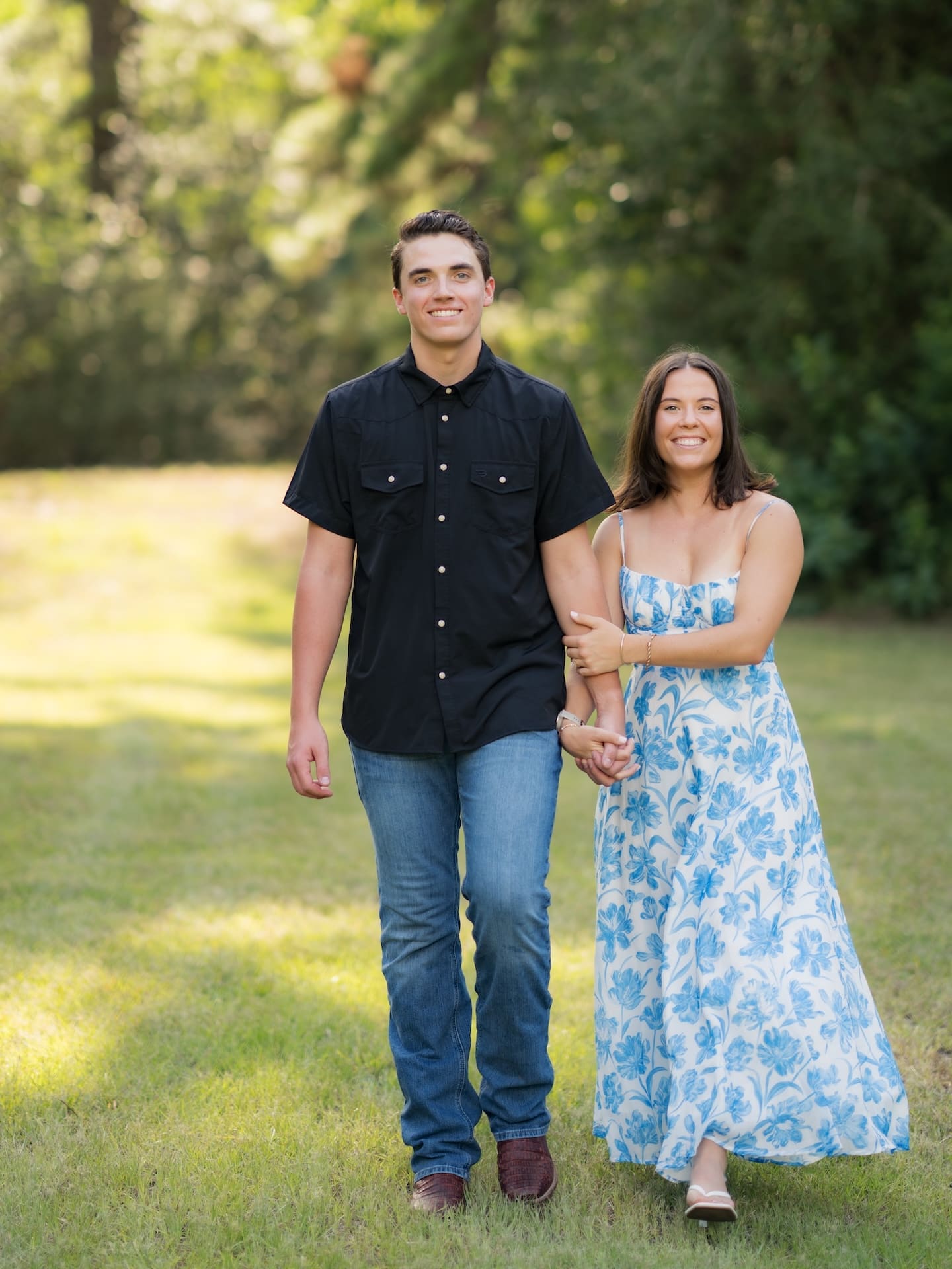 Couple smiling and walking arm in arm across a sunlit grassy field.