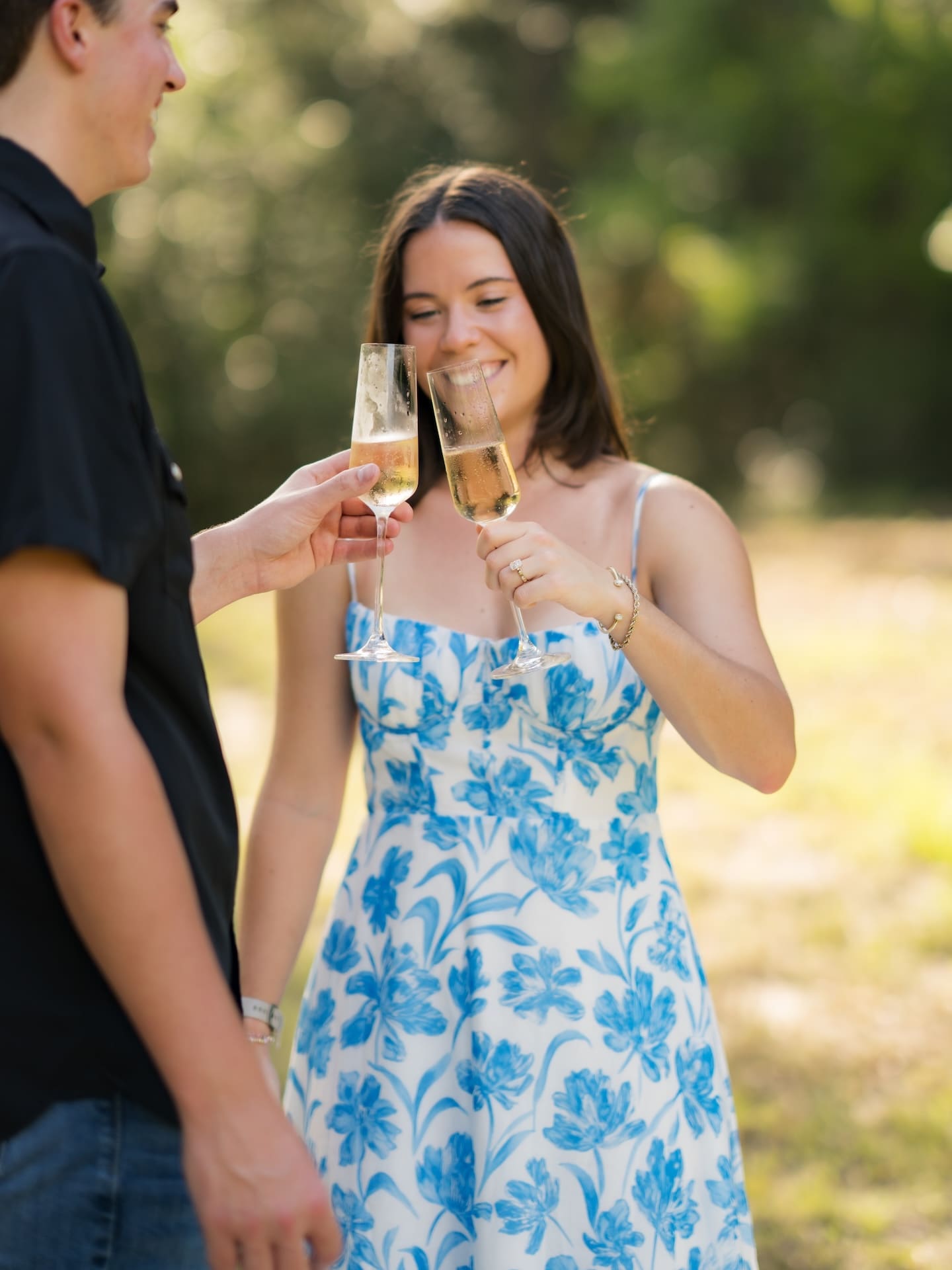 Newly engaged couple toasting champagne glasses together outdoors.