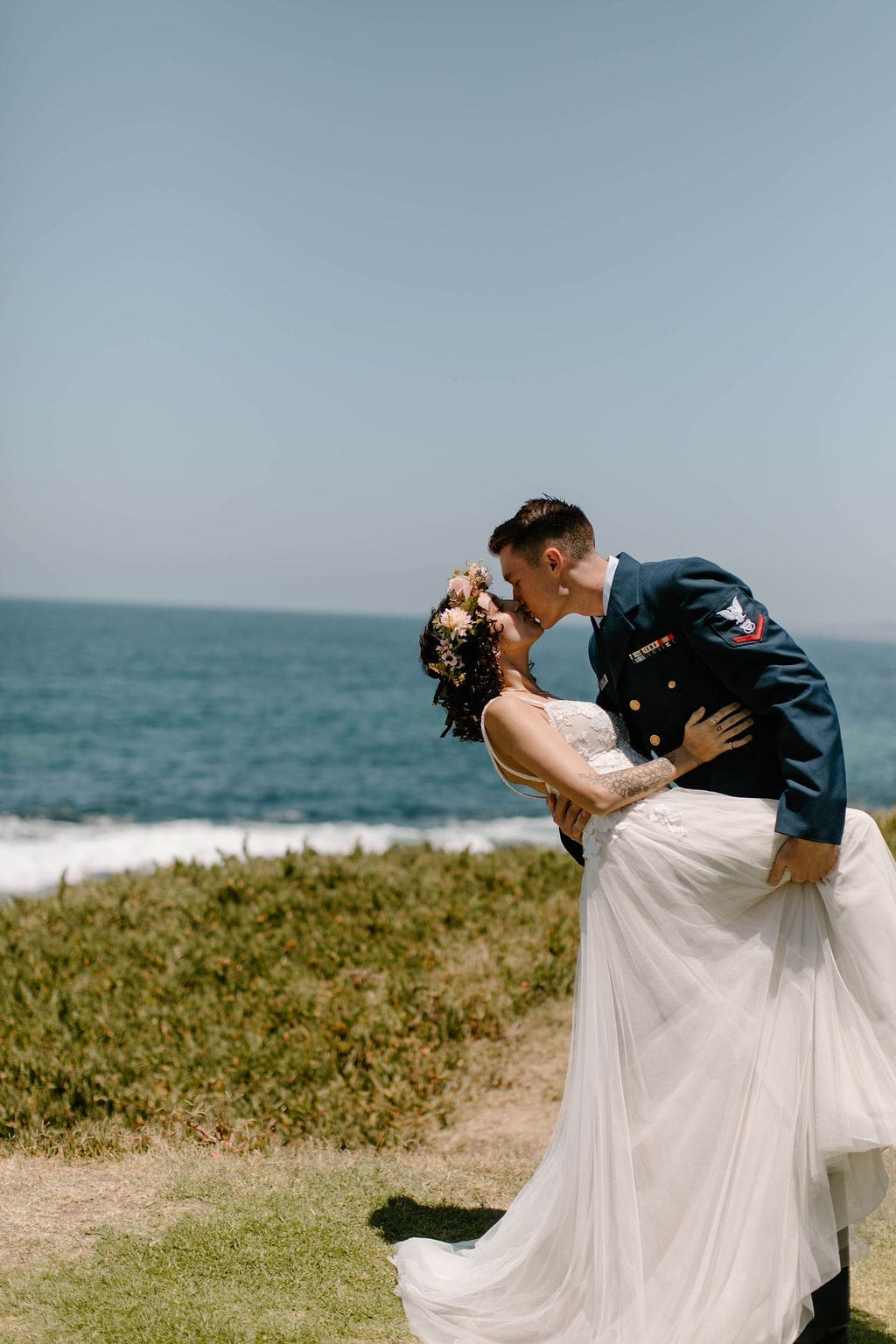A sweeping dip kiss on the grassy bluff above the water, her tulle skirt catching the breeze during their California elopement.