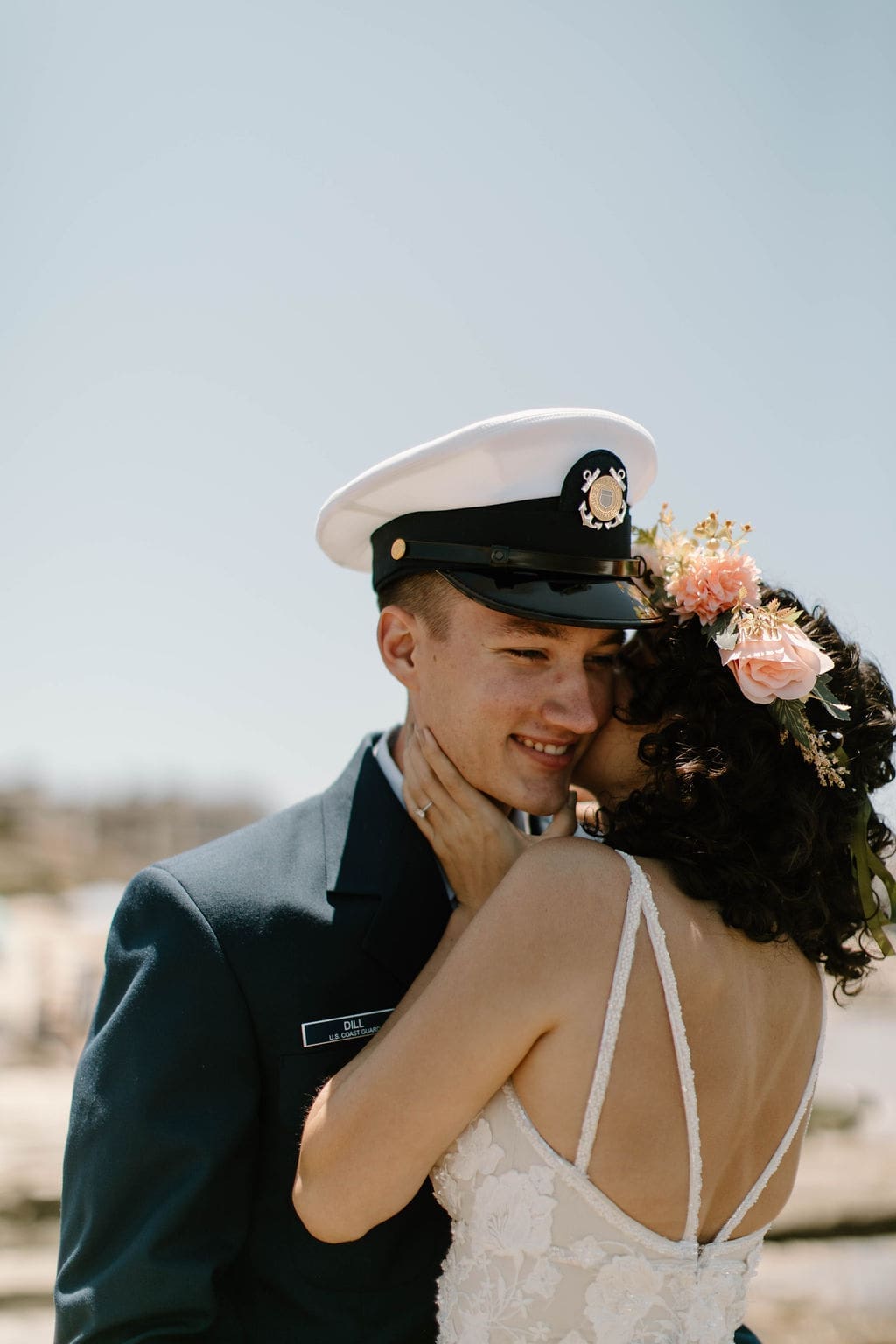 Groom cups his bride's face for a kiss on the beach, ocean stretching calm and blue behind them, a quiet high point of their California elopement.