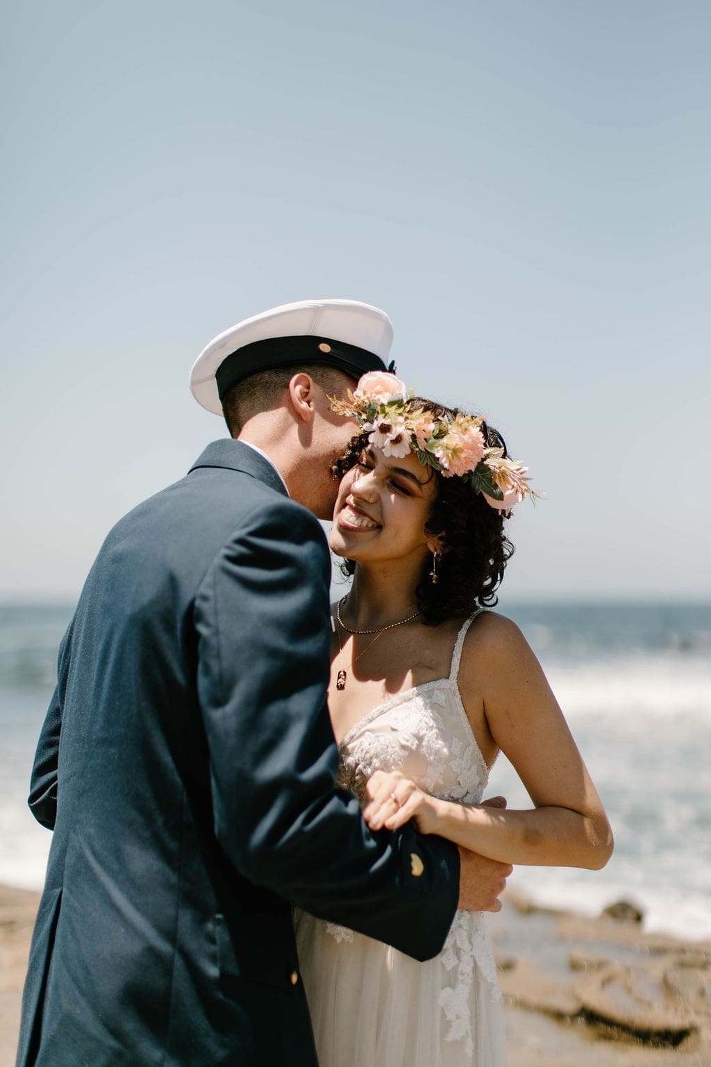 Groom twirls his bride under his arm on the sand, her flower crown and gown catching the sun.