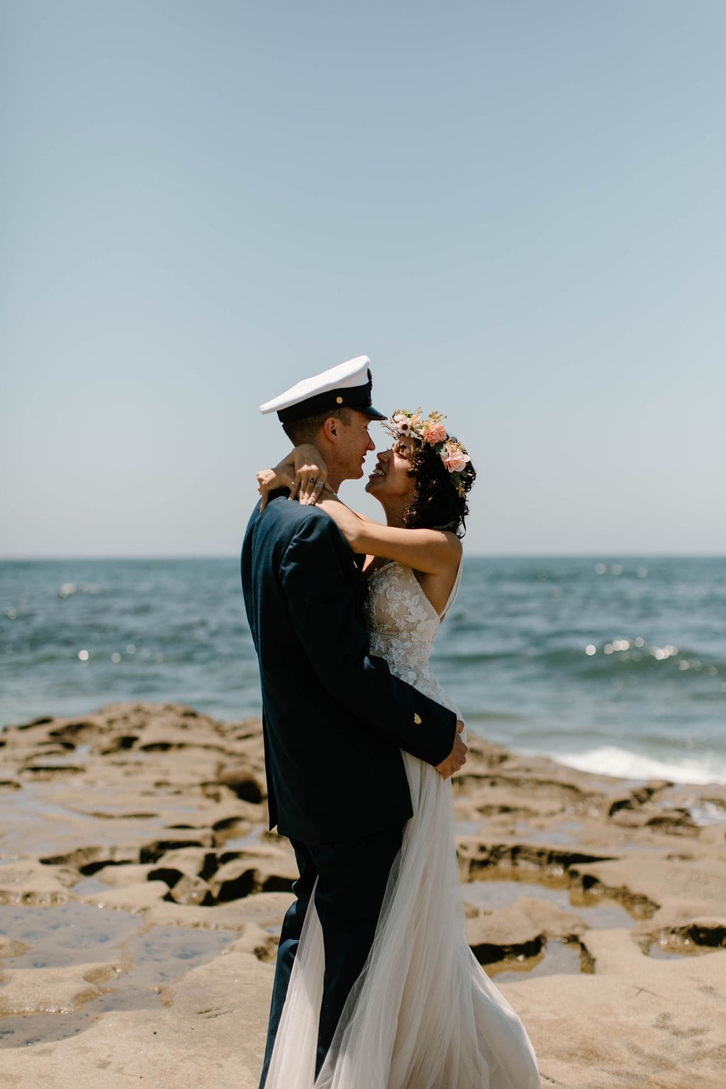 Groom twirls his bride under his arm on the sand, her flower crown and gown catching the sun.