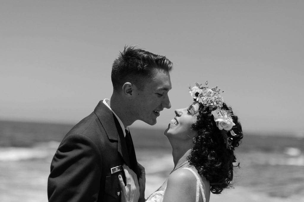 Black and white close-up of the two of them nose to nose, both grinning, ocean stretching out behind them.