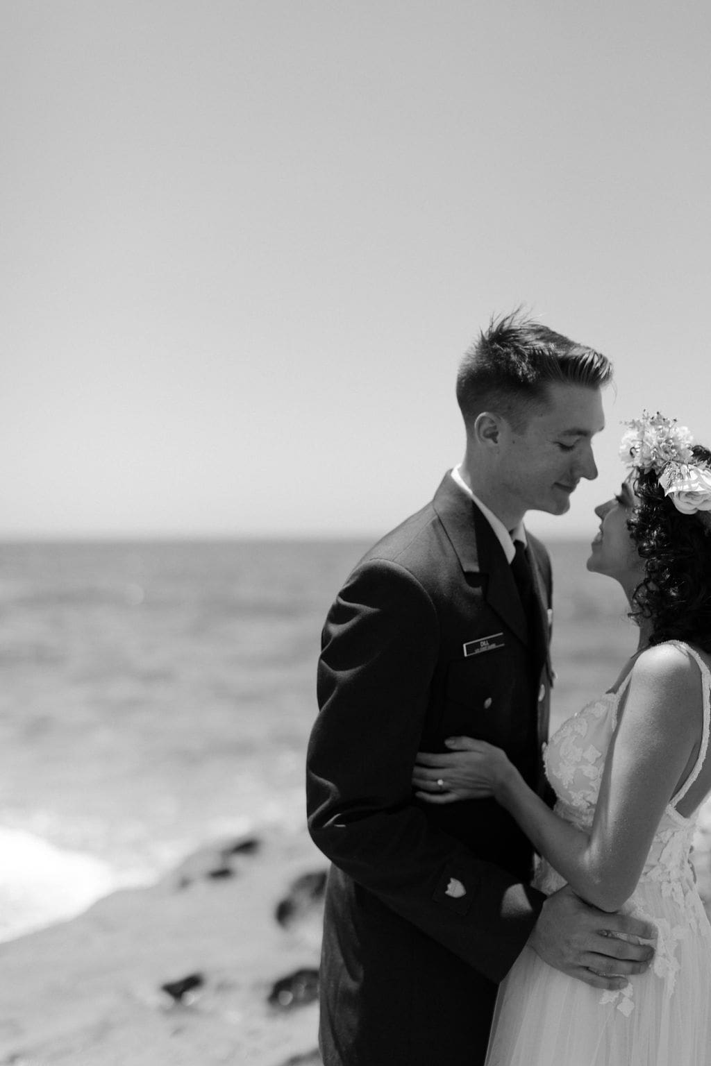 Black and white shot of the couple kissing as sea spray drifts around them on the rocky shore, a striking moment from their California elopement.