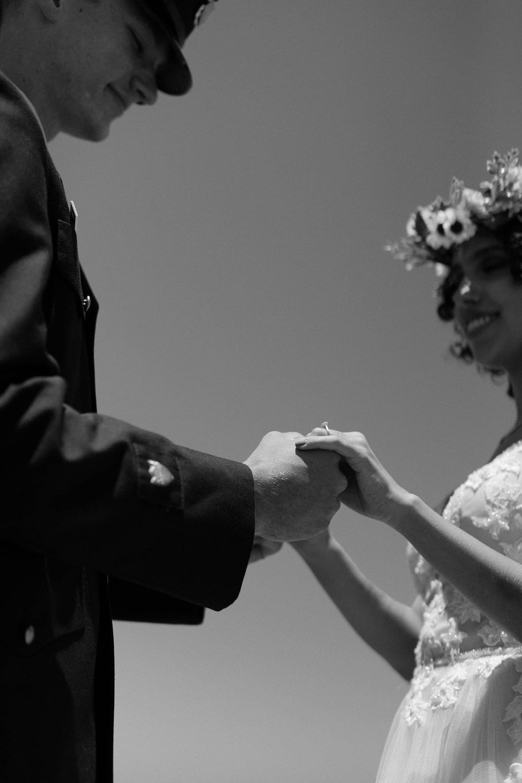 Black and white shot of the couple holding hands mid ceremony, her ring catching the light as she smiles up at him, a tender beat from their California elopement.