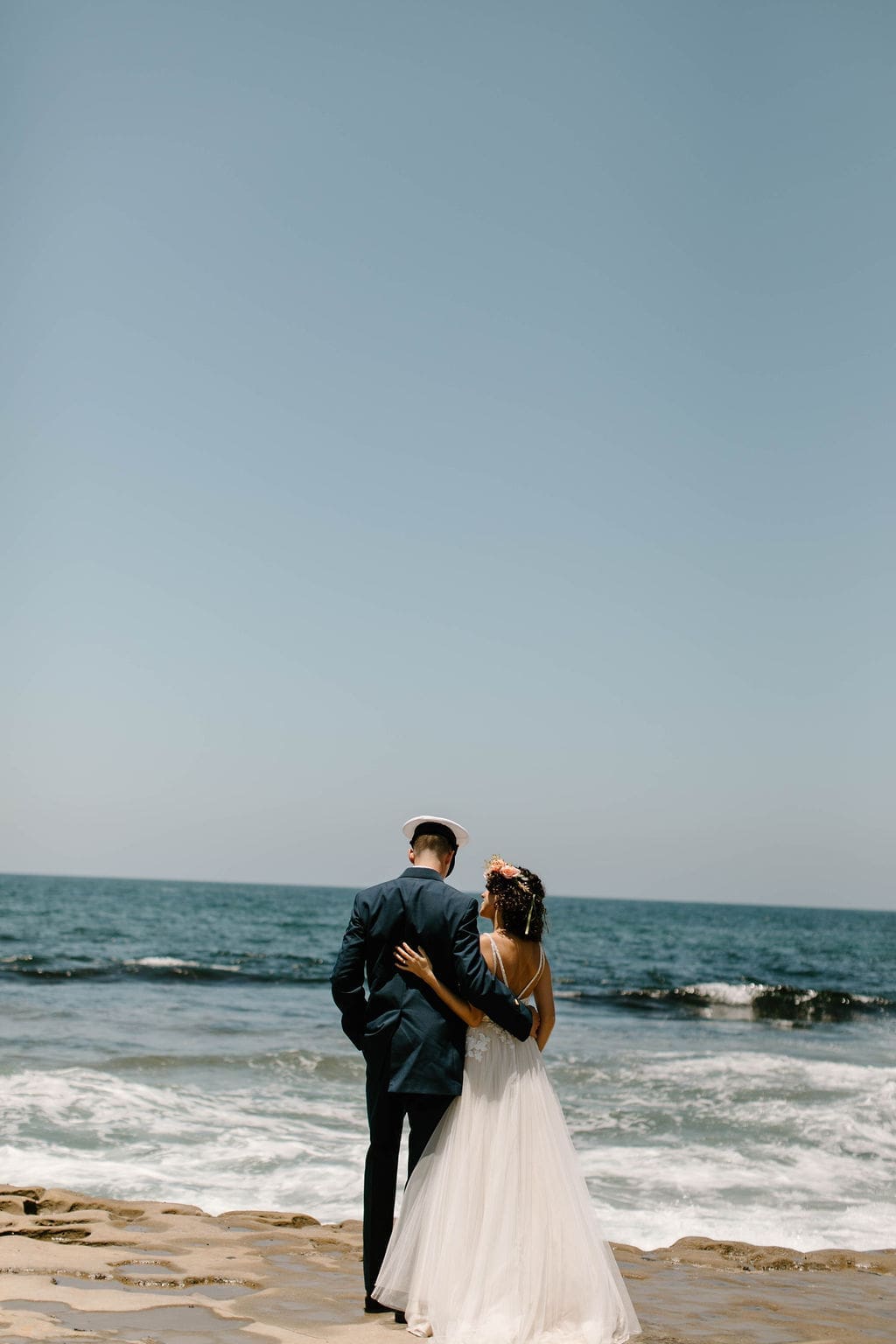 From behind, the newlyweds stand arm in arm gazing out at the open ocean, a quiet close to their California elopement.
