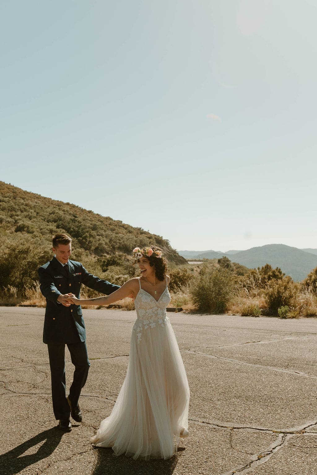 Groom twirls his laughing bride on a mountain road, hills fading into the distance behind them.