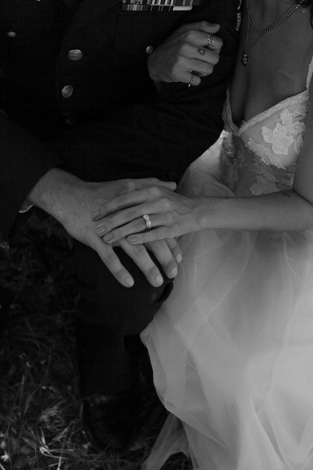 Black and white close up of intertwined hands resting on her tulle skirt, his dress uniform ribbons visible above.