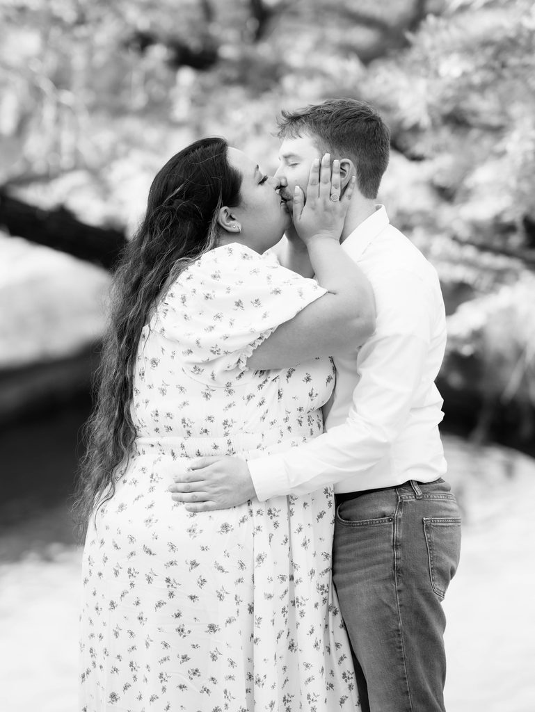 Black-and-white close-up of couple kissing, woman's hand resting on man's cheek, engagement ring visible — a tender detail shot from one of the day's Engagement Photo Locations.
