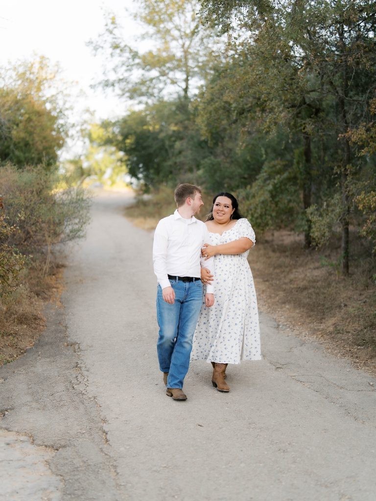 Couple walking arm-in-arm down a tree-lined path, one in cowboy boots, a relaxed choice among Engagement Photo Locations.