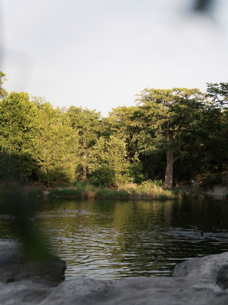 Tranquil river swimming hole surrounded by lush green trees, with swimmers visible in the water — a scenic natural Engagement Photo Locations pick.