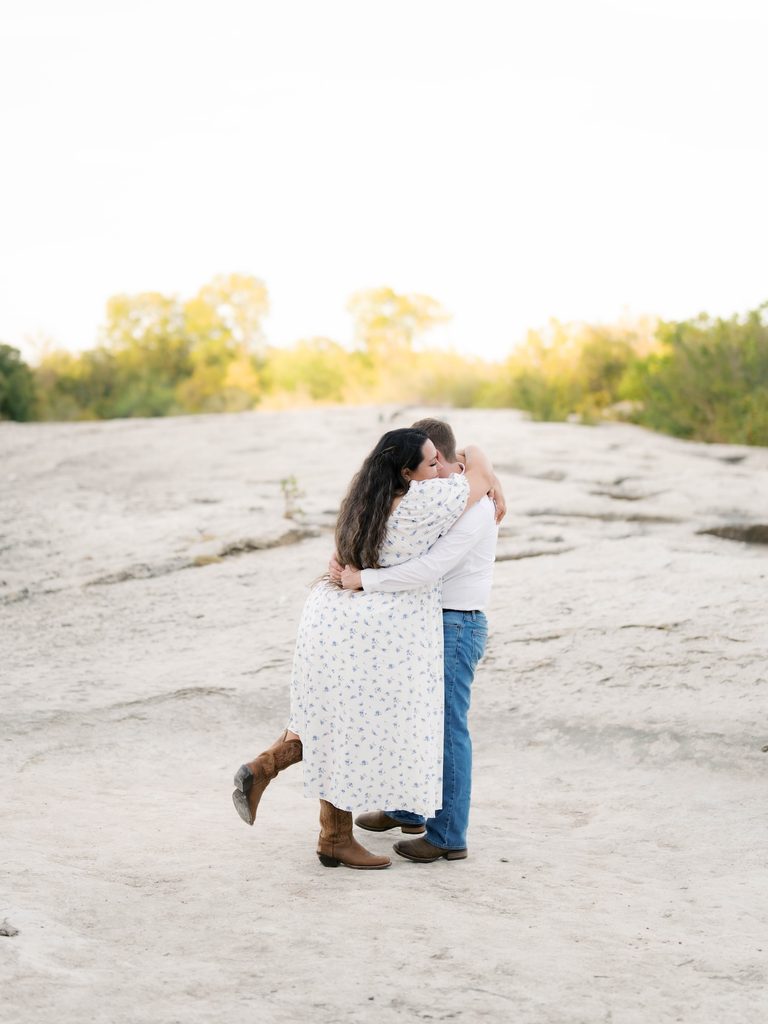 Couple embracing on a wide limestone rock formation surrounded by trees, a scenic natural pick among Engagement Photo Locations.
