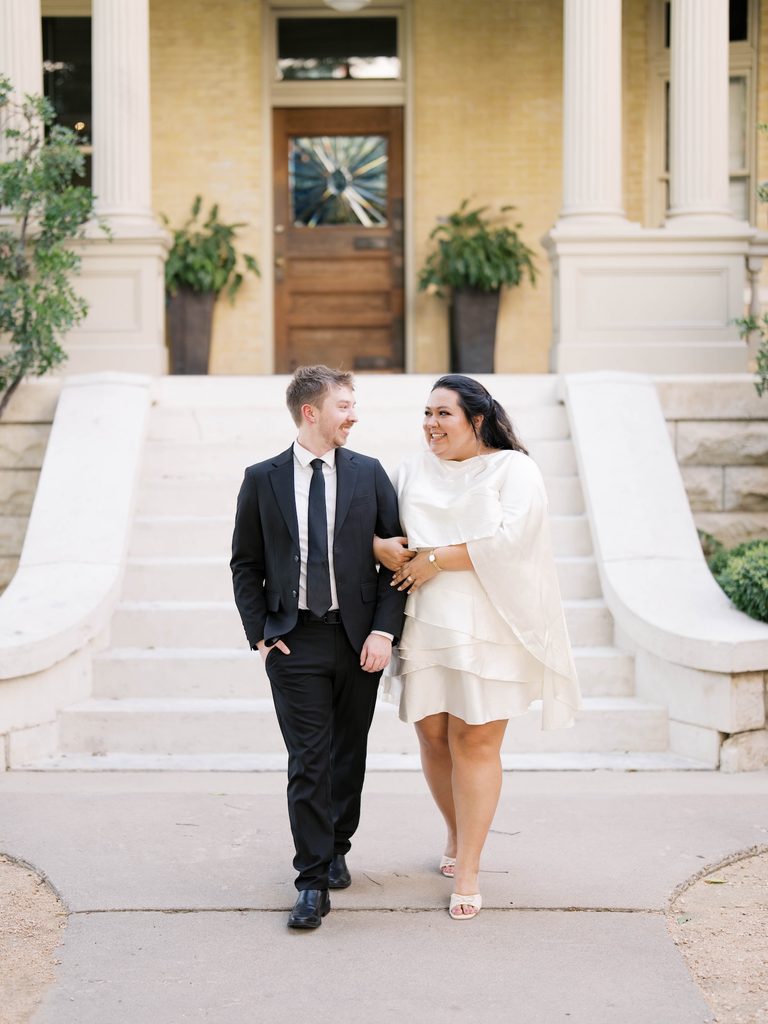 Couple walking arm-in-arm in front of a historic mansion's grand staircase and columns, a standout among Engagement Photo Locations.