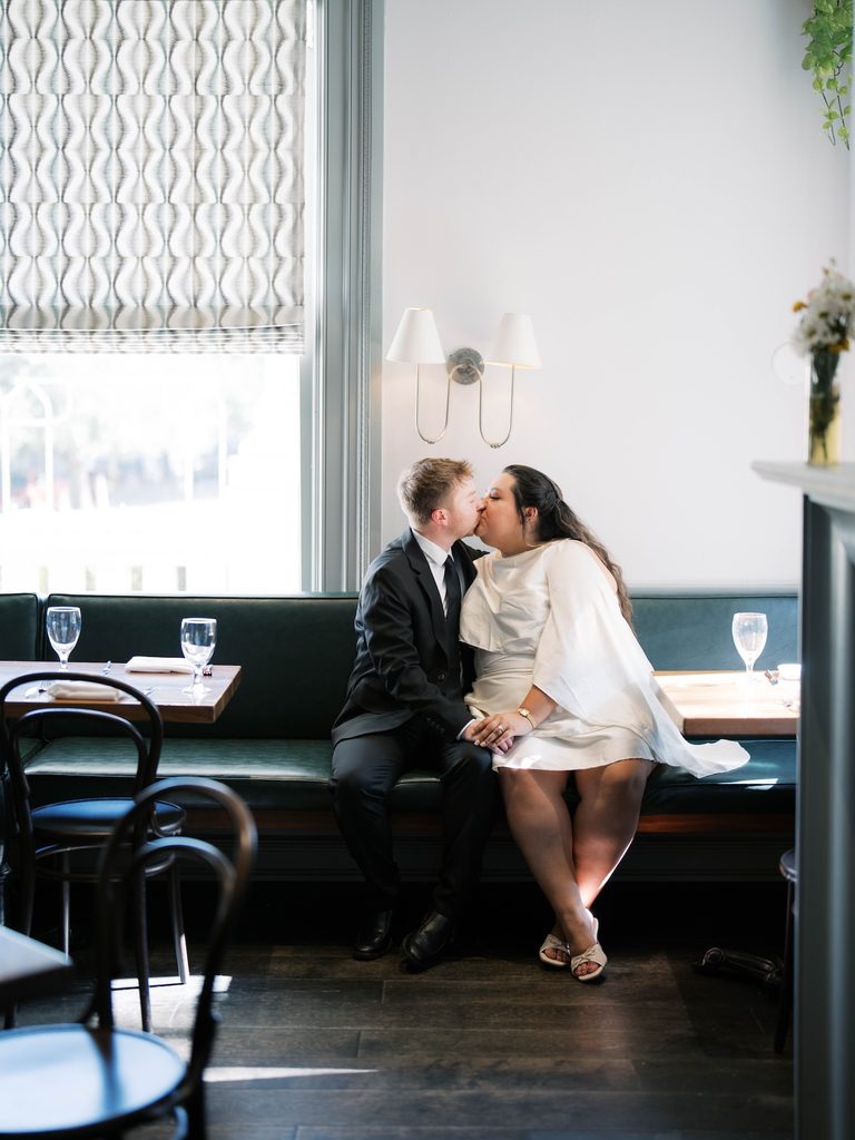 Couple kissing while seated together in a cozy restaurant booth, one of the more intimate indoor Engagement Photo Locations.