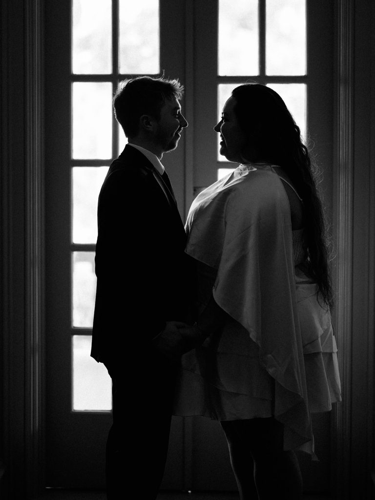 Silhouetted couple facing each other in front of tall paned French doors, a moody indoor pick among Engagement Photo Locations.
