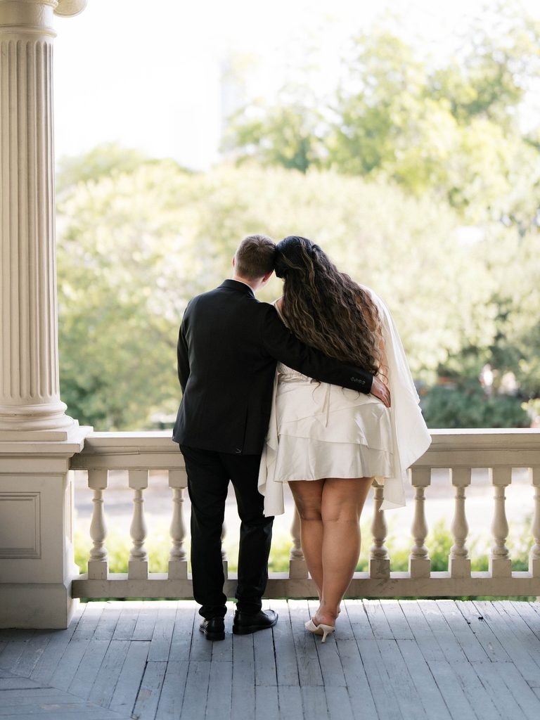 Back view of couple leaning on a balcony railing with foreheads touching, framed by greenery — a romantic pick among Engagement Photo Locations.
