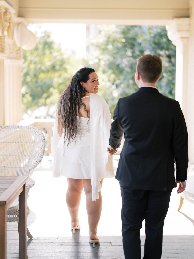 Couple walking hand-in-hand across a covered porch, bride glancing back and smiling — a charming example of Engagement Photo Locations with vintage character.