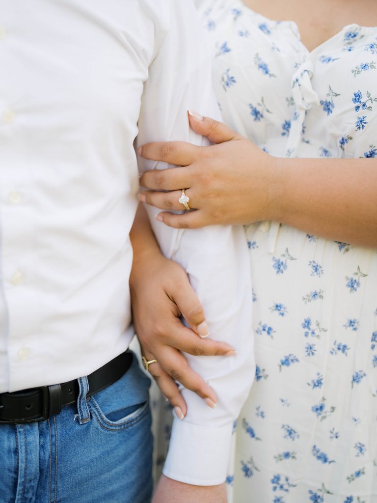 Close-up of couple's arms linked together, engagement ring visible against a blue floral dress.