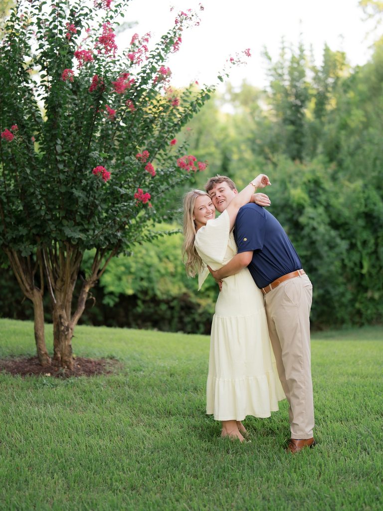 Playful, candid hug between a newly engaged couple on the grass, captured at their Brenners on the Bayou proposal session